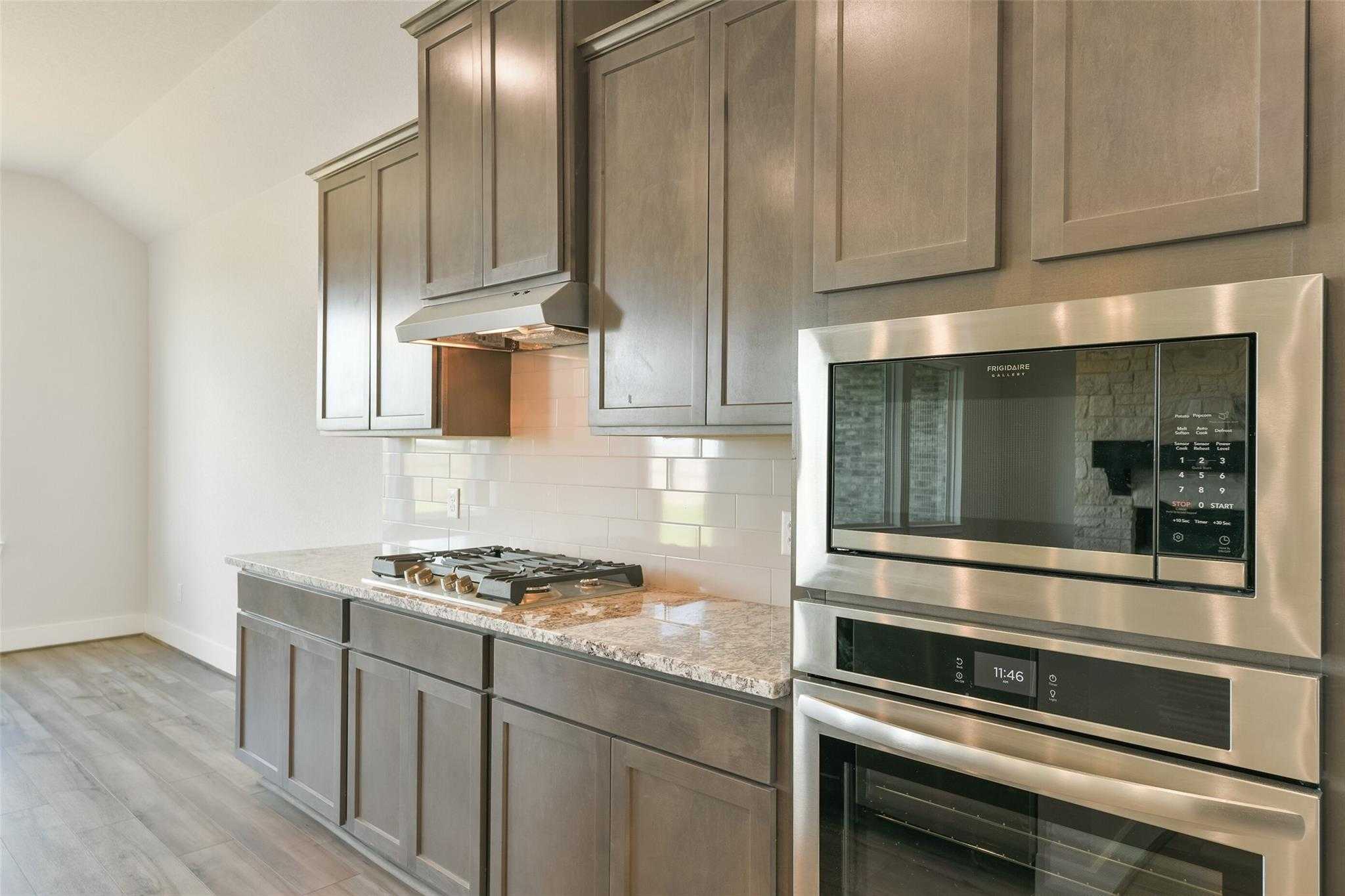 Modern kitchen featuring gray shaker cabinets, granite countertops, stainless steel oven and cooktop in Davidson Homes The Edward A, Lago Mar, Texas City