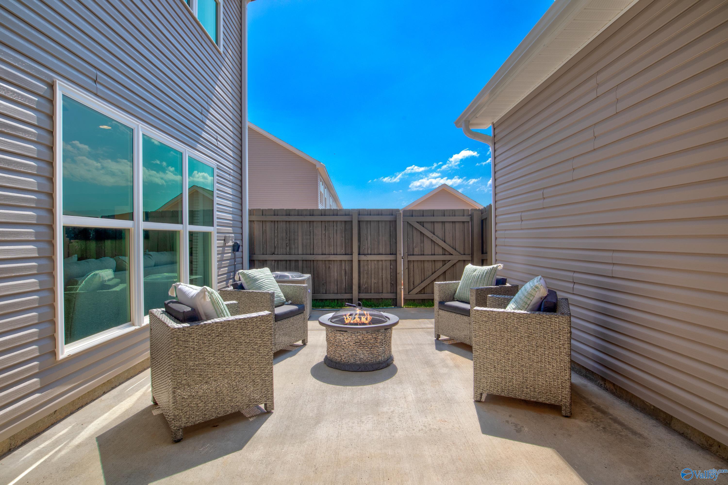 Cozy backyard patio with wicker chairs around stone fire pit, wooden fence in Davidson Homes The Covington C, Decatur, Alabama