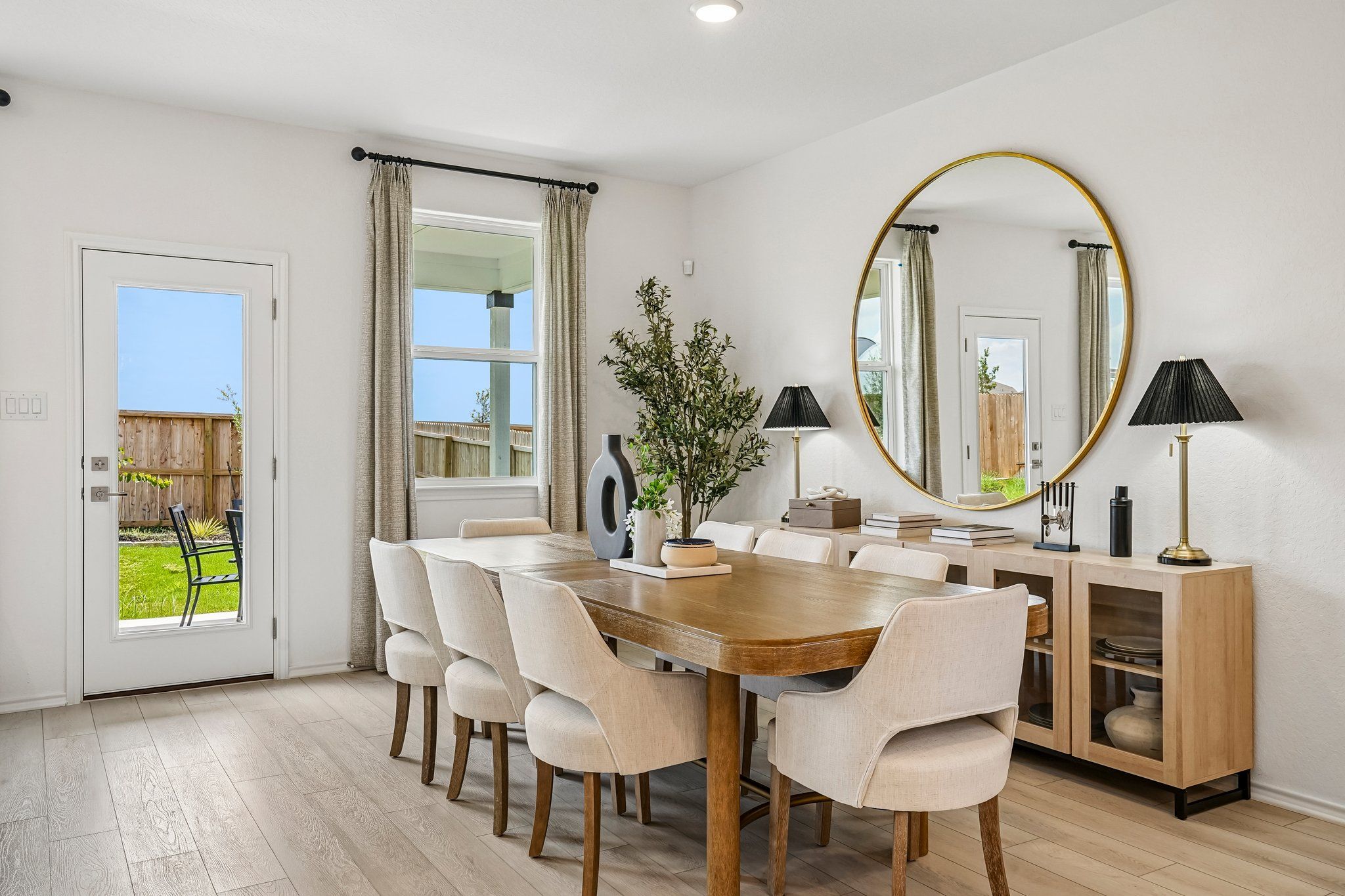 Modern dining room at Morgan Meadows in San Antonio with wooden table, upholstered chairs, and large round gold mirror.