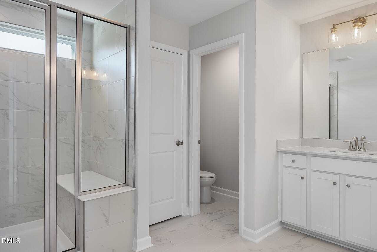 Modern master bathroom with frameless glass shower, marble tile accents, white vanity sink, and separate toilet in Davidson Homes The Graham, Fuquay-Varina, NC