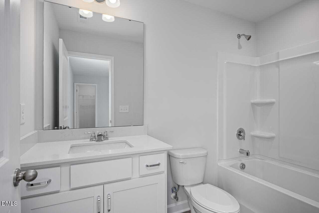 Modern white bathroom featuring double-sink vanity, large mirror, tub-shower combo in Davidson Homes Hickory II B, Zebulon, NC