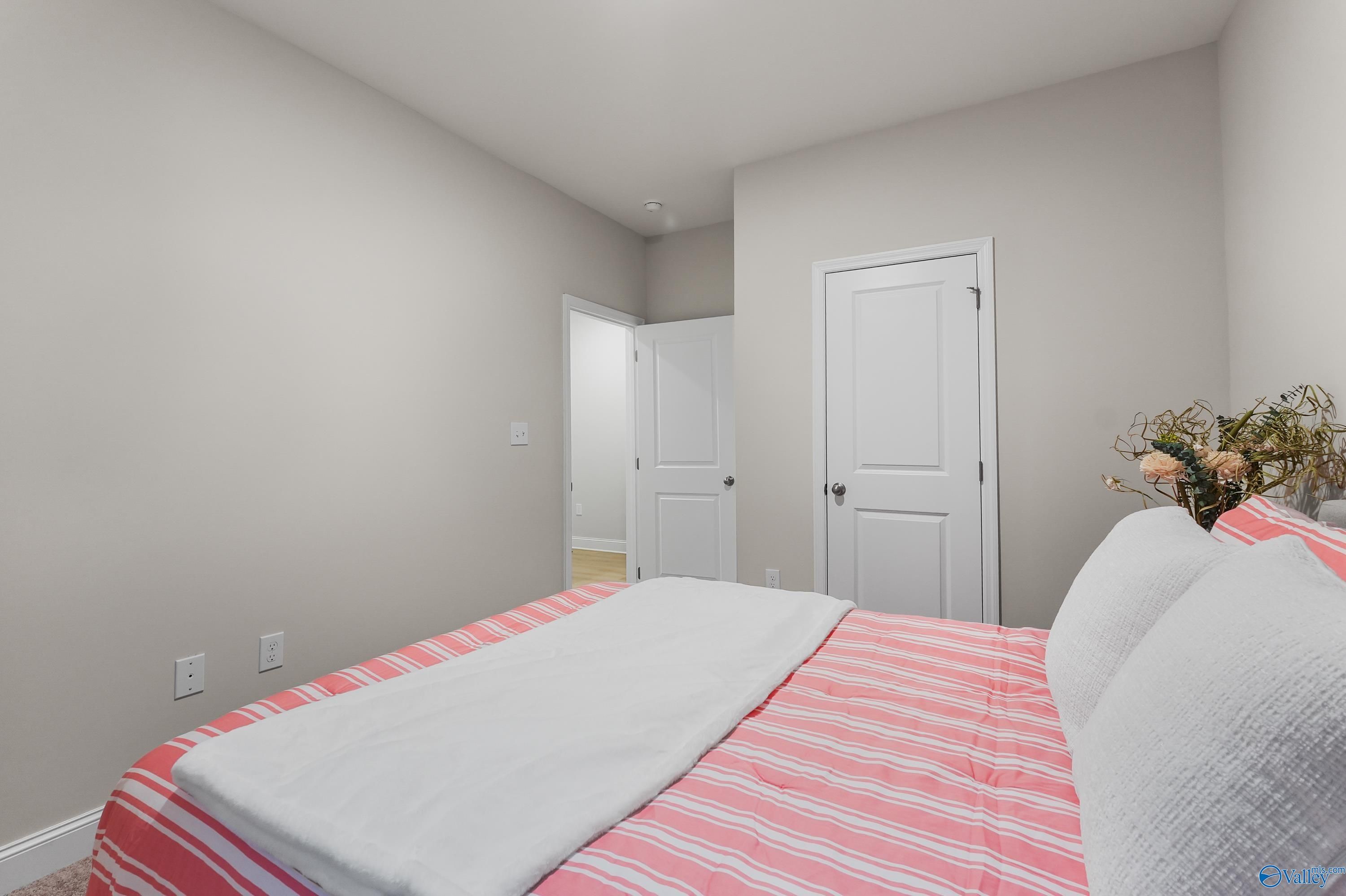 Cozy bedroom with pink striped bedding, white pillows, and light gray walls in Davidson Homes The Asheville C, Huntsville AL