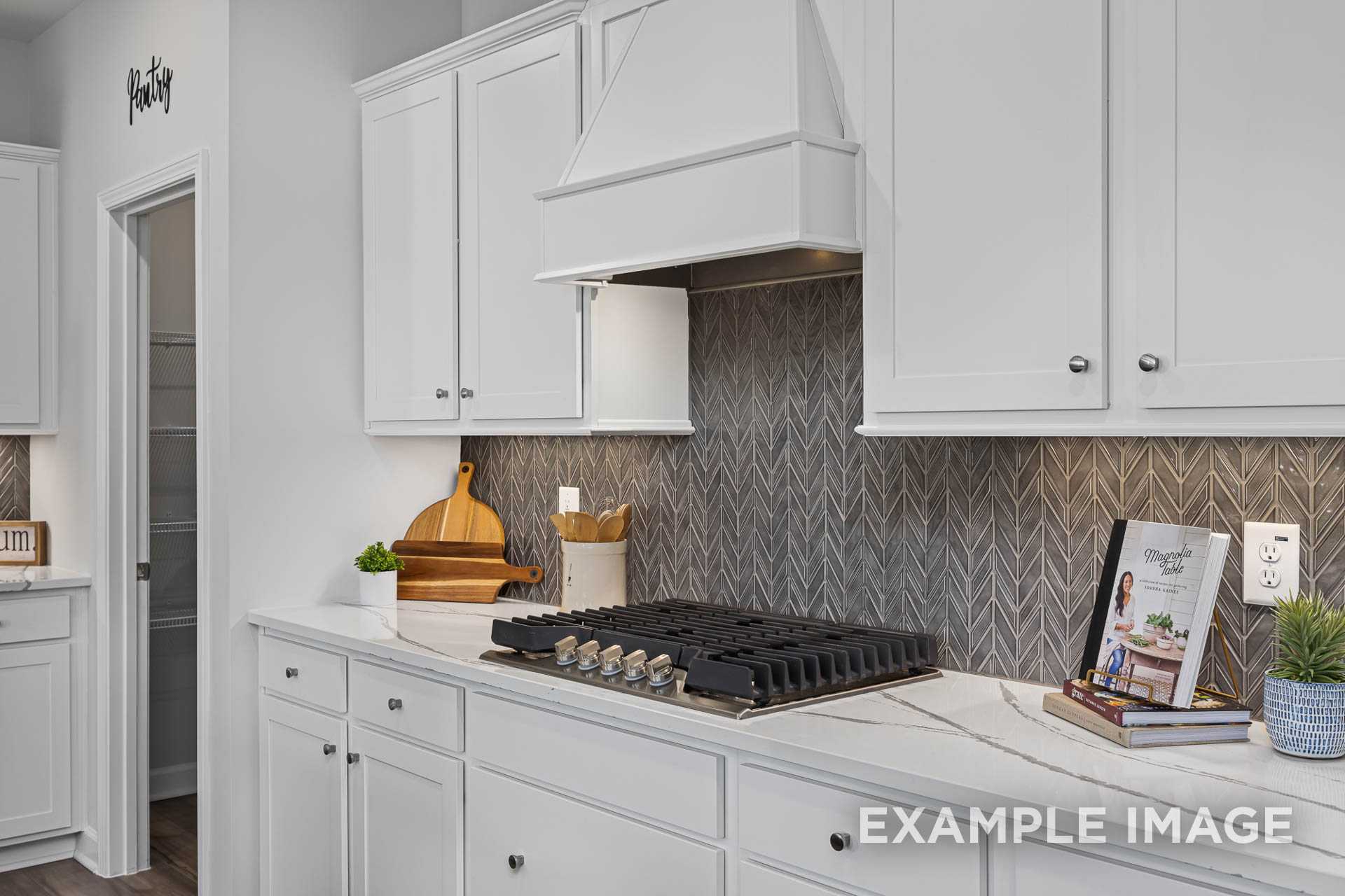 Spacious kitchen in The Adalynn A with white shaker cabinets, herringbone gray backsplash, gas range, and quartz counters