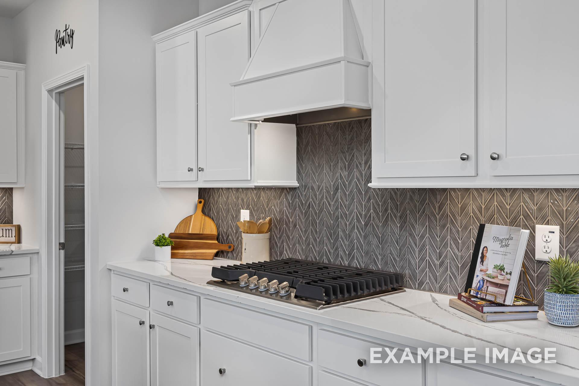 Modern kitchen in The Adalynn C with white shaker cabinets, gas range, herringbone subway tile backsplash, and quartz counters