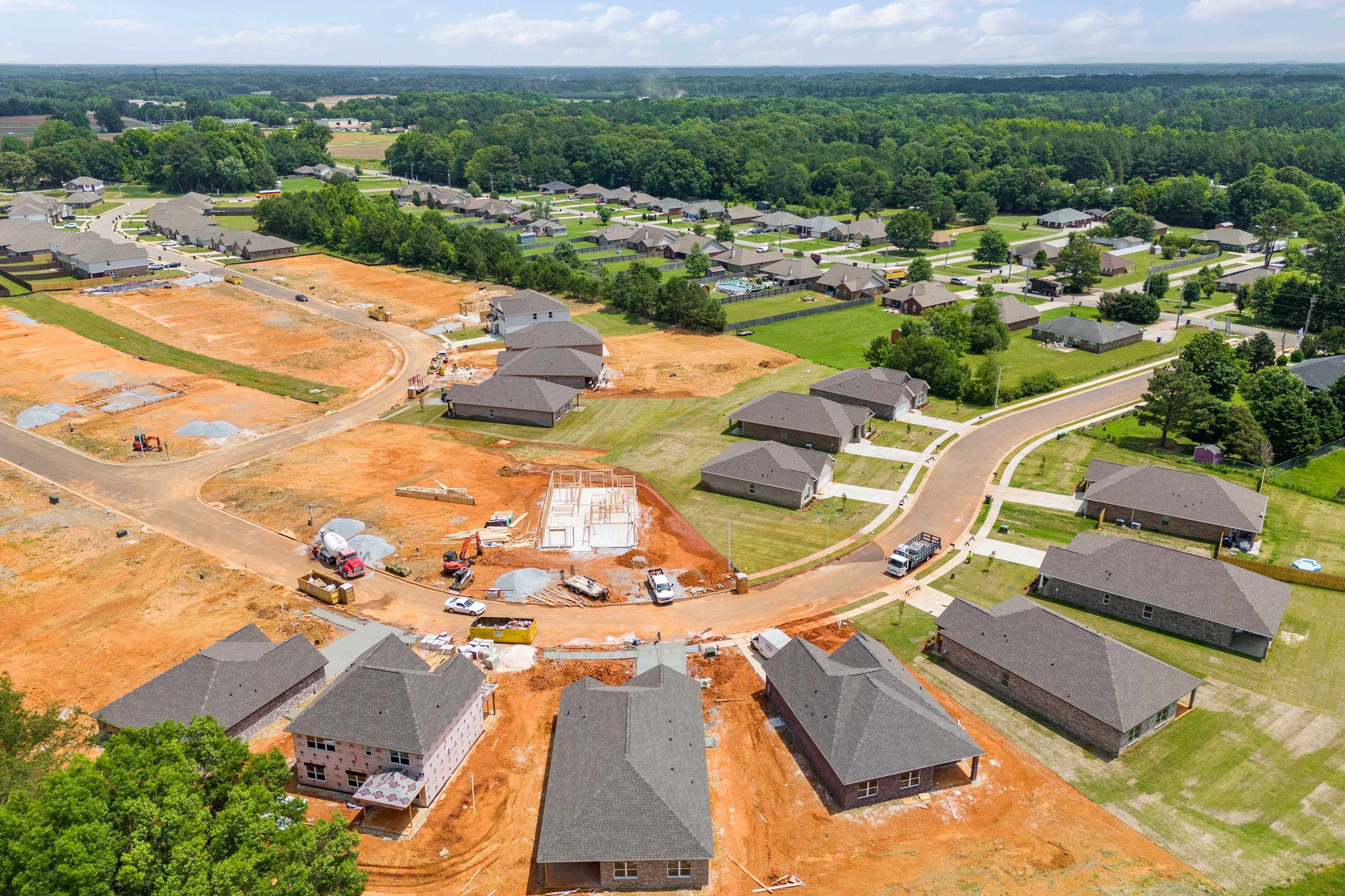 Aerial view of Durham Farms in Harvest Alabama showing new homes under construction amid dirt roads, green lots, and wooded surroundings