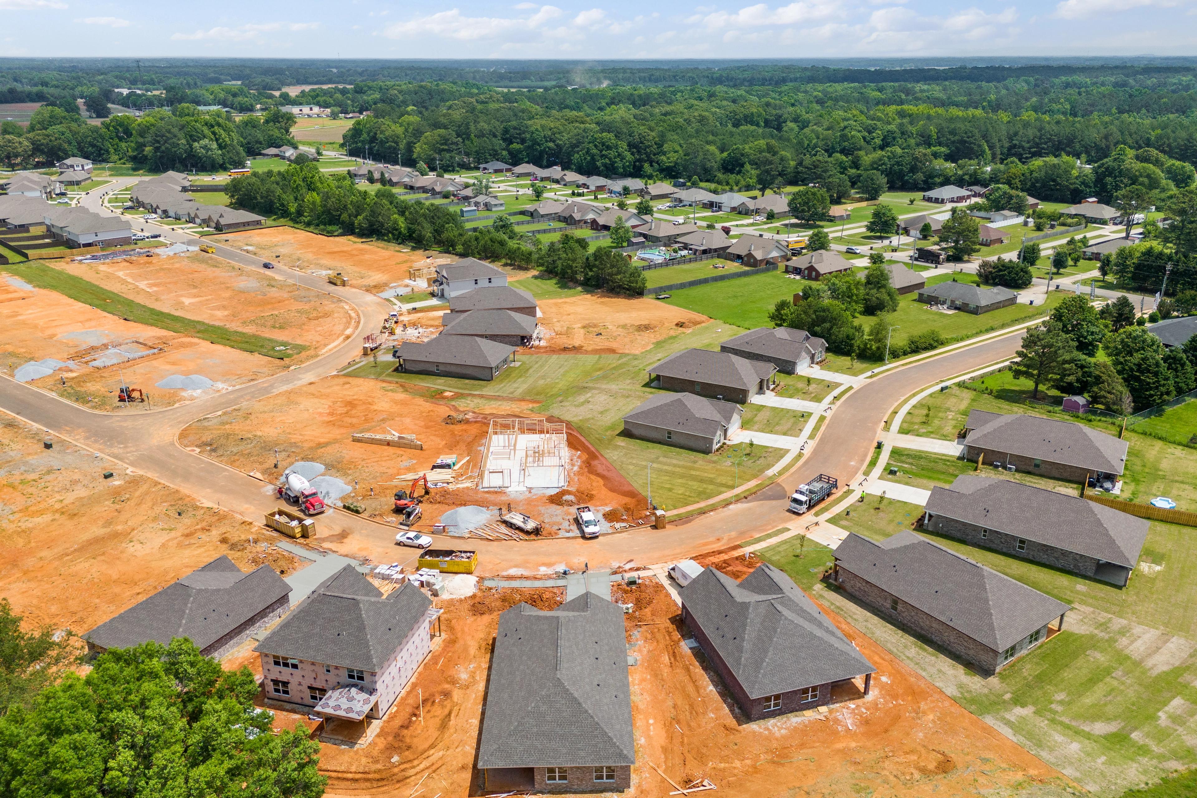Aerial view of Durham Farms in Harvest Alabama showing new homes under construction amid dirt roads, green lots, and wooded surroundings