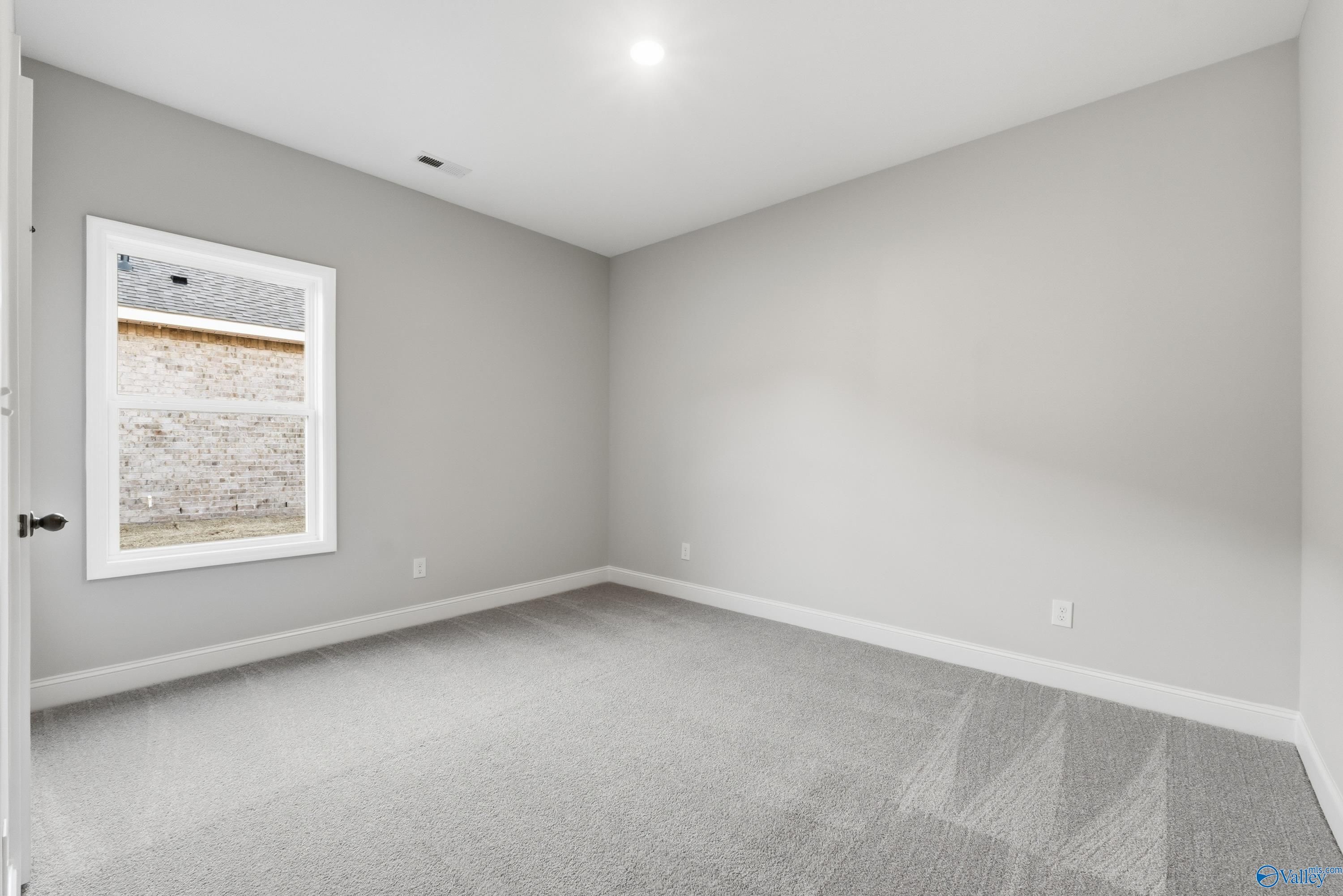 Spacious empty bedroom with light gray walls, plush gray carpet, and large window in Davidson Homes The Daphne C, Athens, Alabama