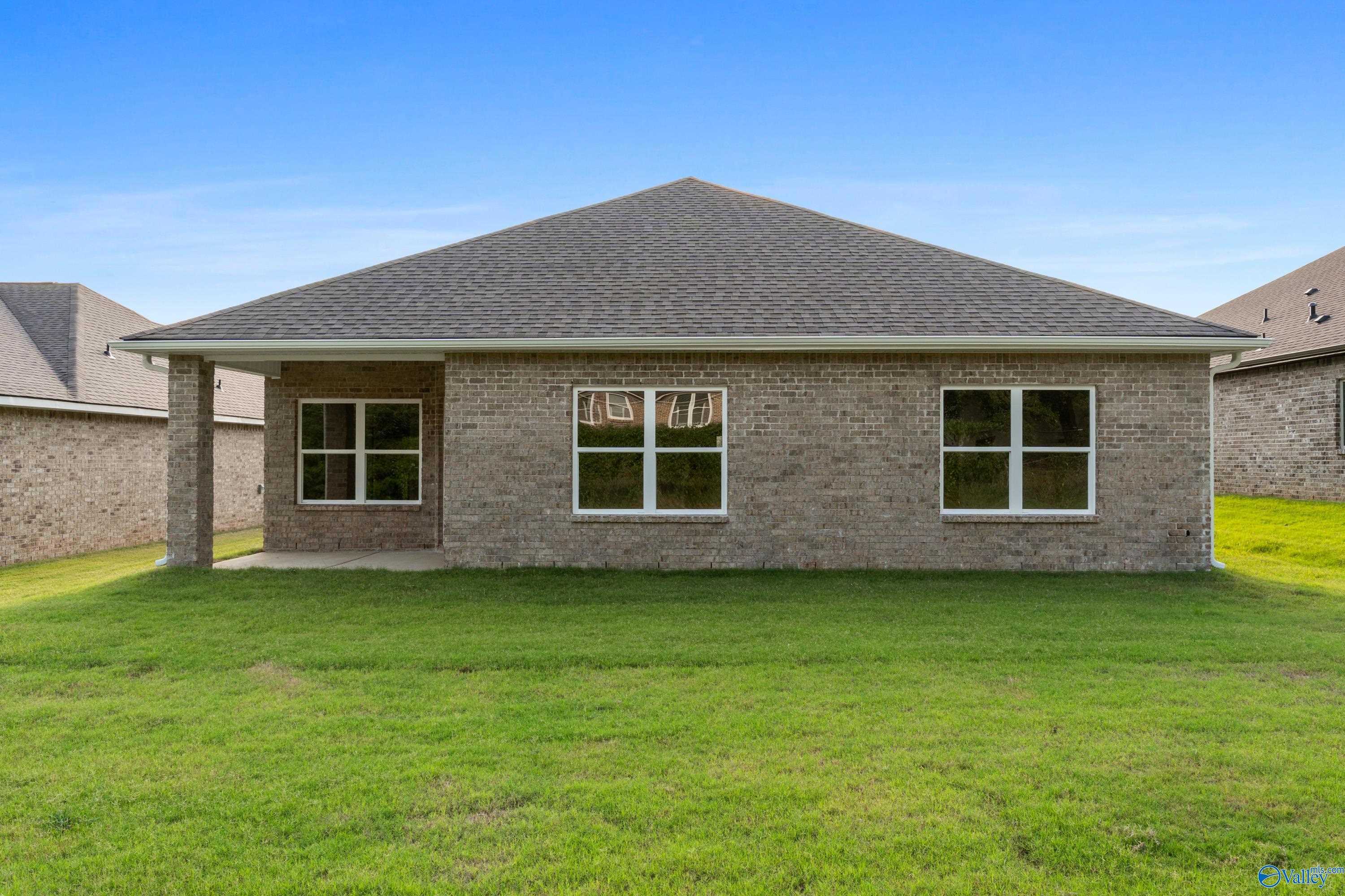 Back view of brick single-story home with covered patio, large windows, and green lawn in Jaguar Hills, Huntsville, Alabama