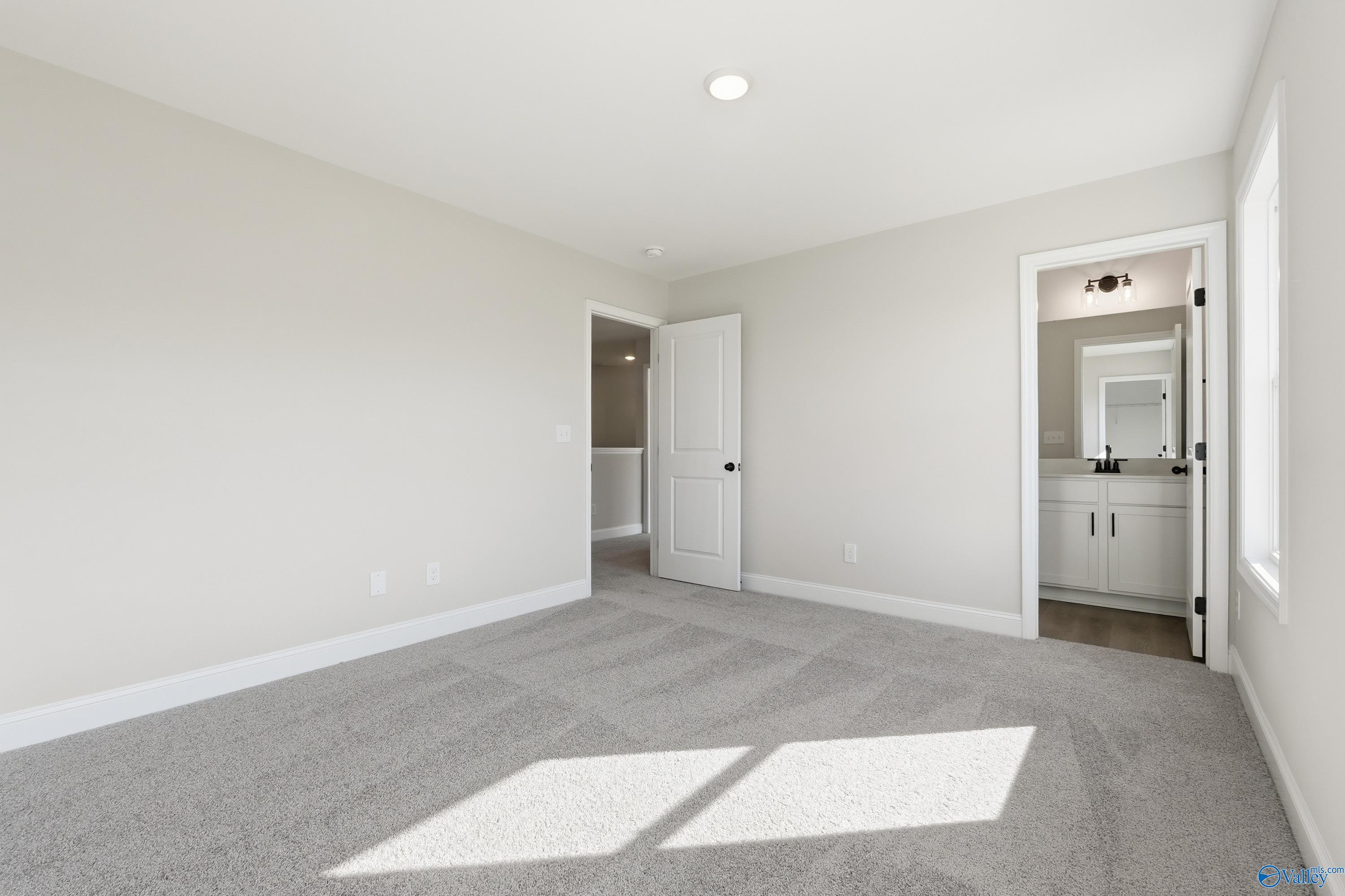 Bright bedroom with attached bathroom, beige walls, carpeted floor in Davidson Homes The Chelsea C, Harvest, Alabama