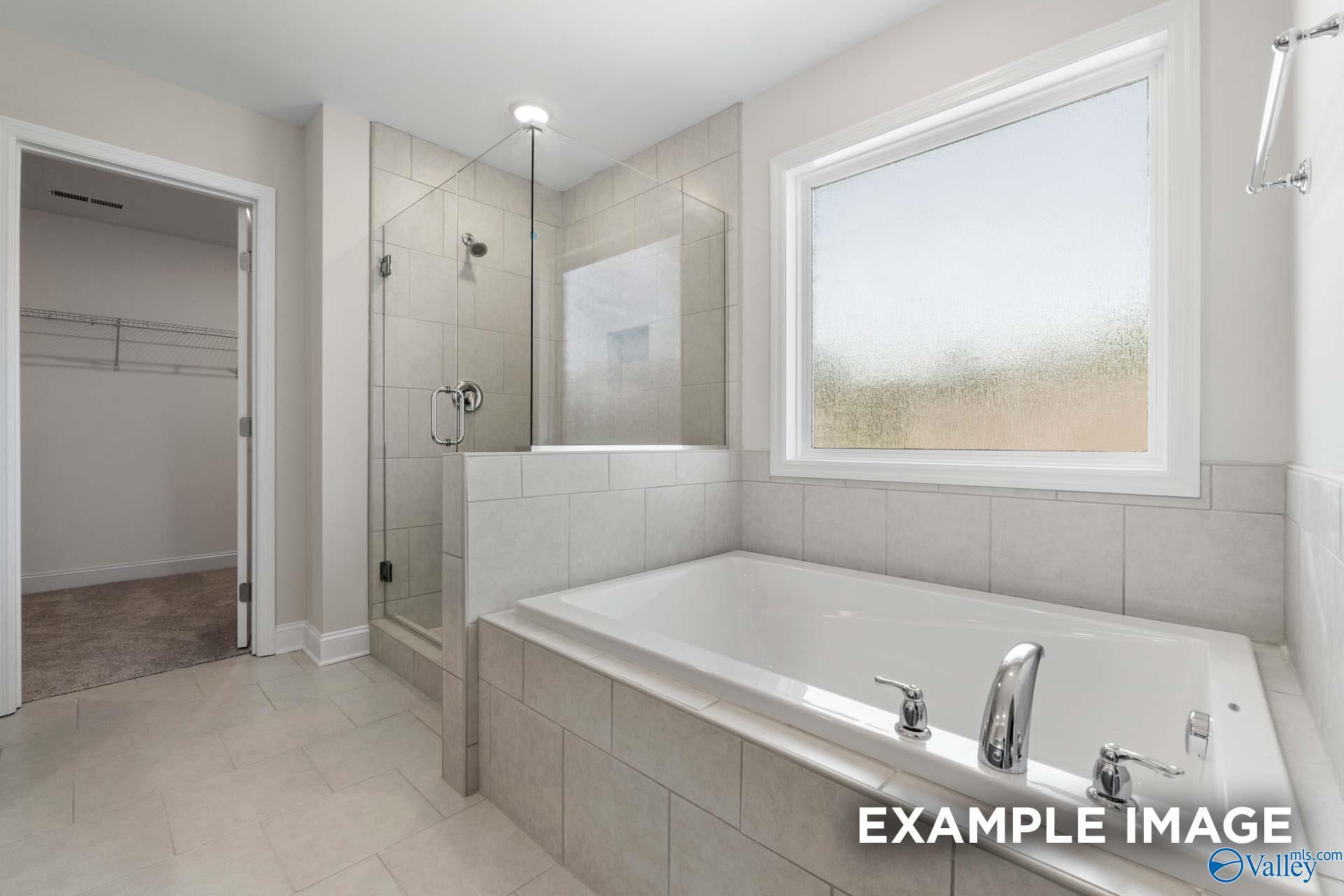 Luxurious master bathroom featuring frameless glass shower, deep soaking tub, and adjacent walk-in closet in Davidson Homes The Madison A, Meridianville, Alabama