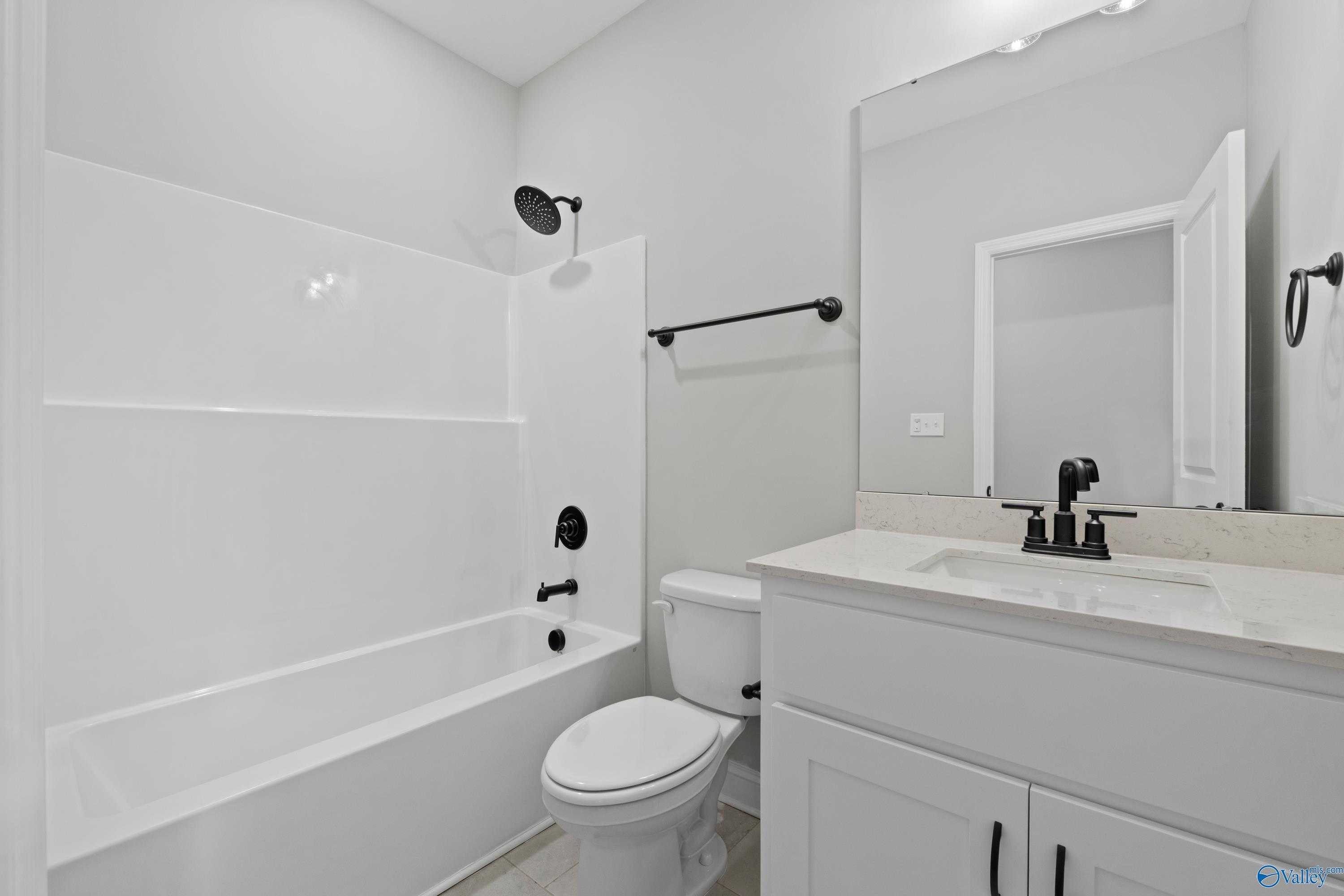 Bright bathroom with white tile tub-shower combo, black fixtures, and quartz vanity in Davidson Homes The Rockford, Toney, Alabama