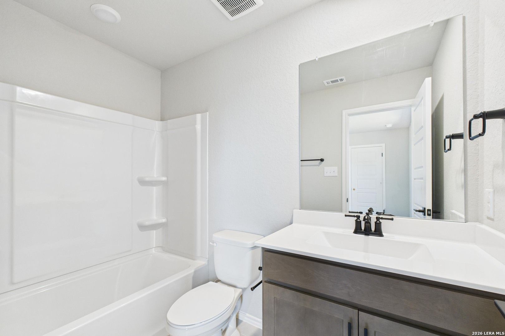 Modern white bathroom with bathtub-shower combo, vanity sink, and large mirror in Davidson Homes The Douglas E, San Antonio