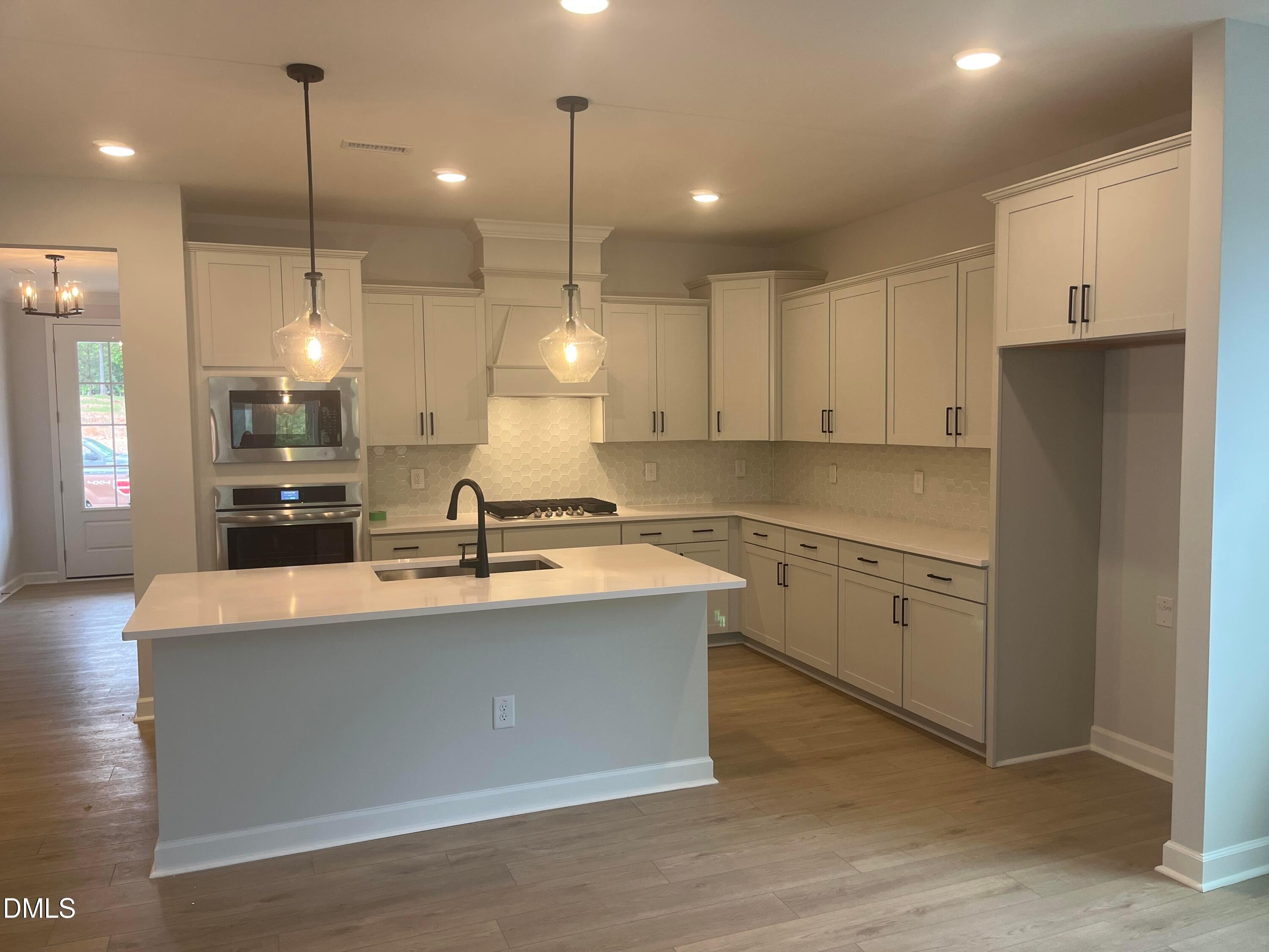 Modern white kitchen with quartz island, stainless steel appliances, subway tile backsplash in Davidson Homes The Birch II E, Wake Forest, NC