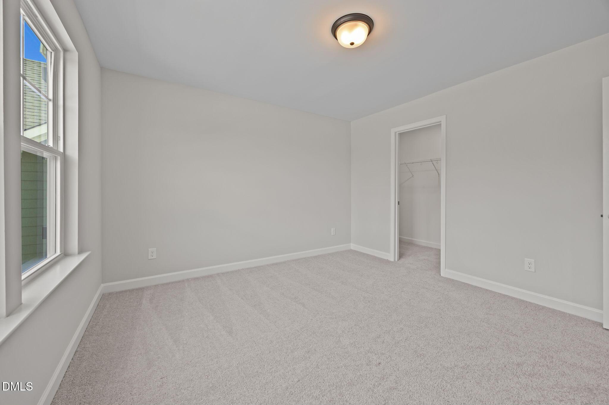 Spacious empty bedroom with plush carpet, large window, and open closet in Davidson Homes The Willow D, Wendell, NC