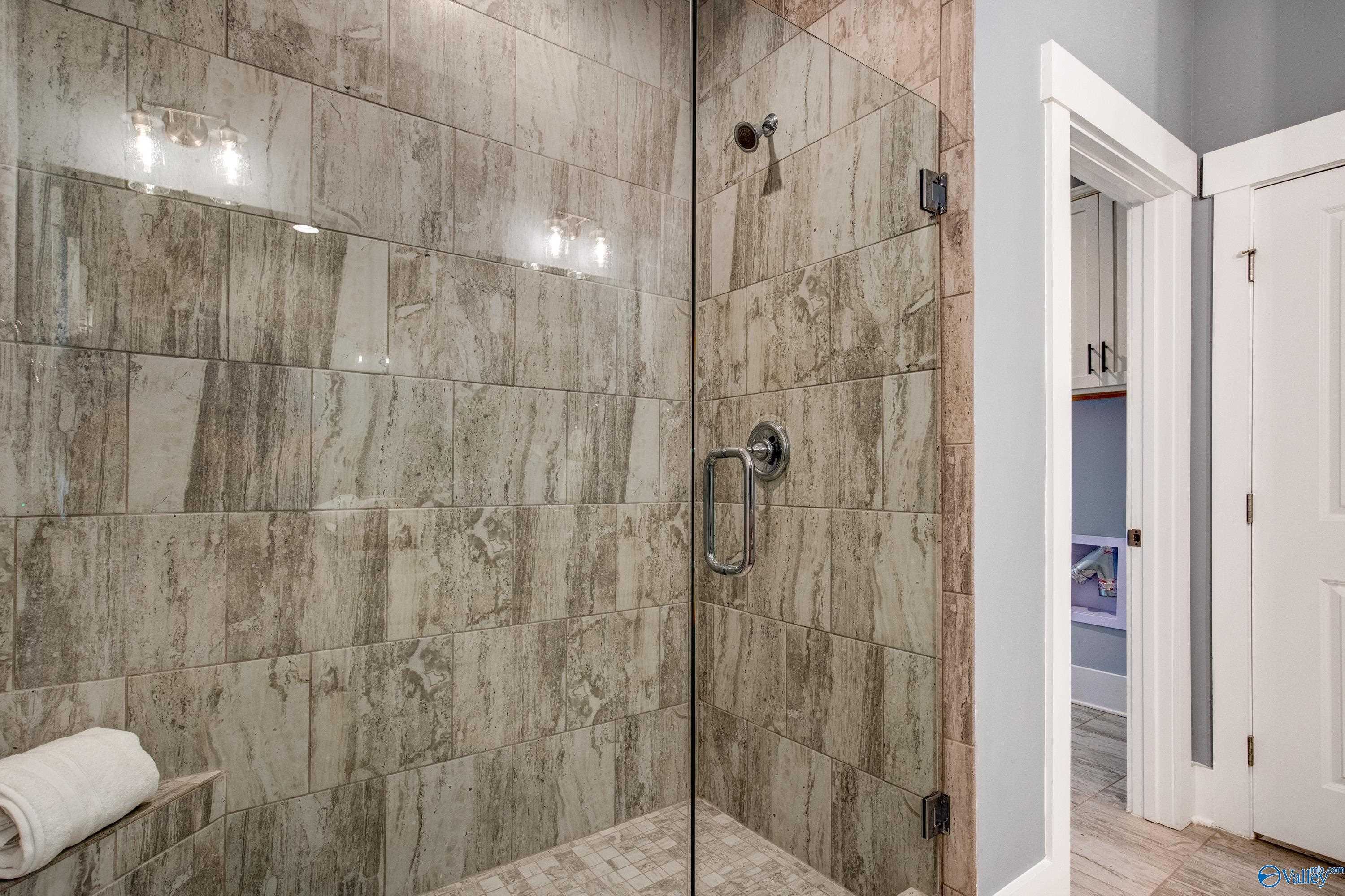 Elegant master bathroom shower with gray subway tiles, frameless glass door, and sconce lighting in Davidson Homes The Covington C, Decatur, Alabama