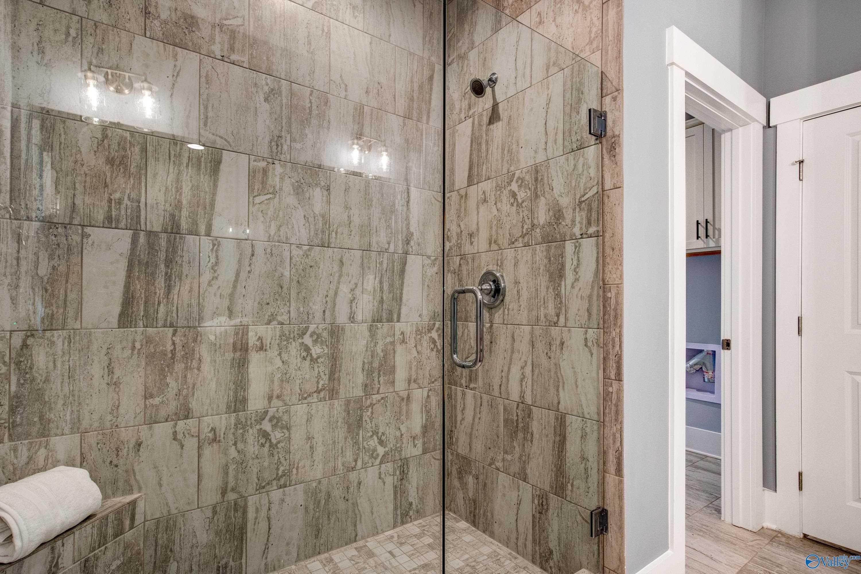 Elegant master bathroom shower with gray subway tiles, frameless glass door, and sconce lighting in Davidson Homes The Covington C, Decatur, Alabama
