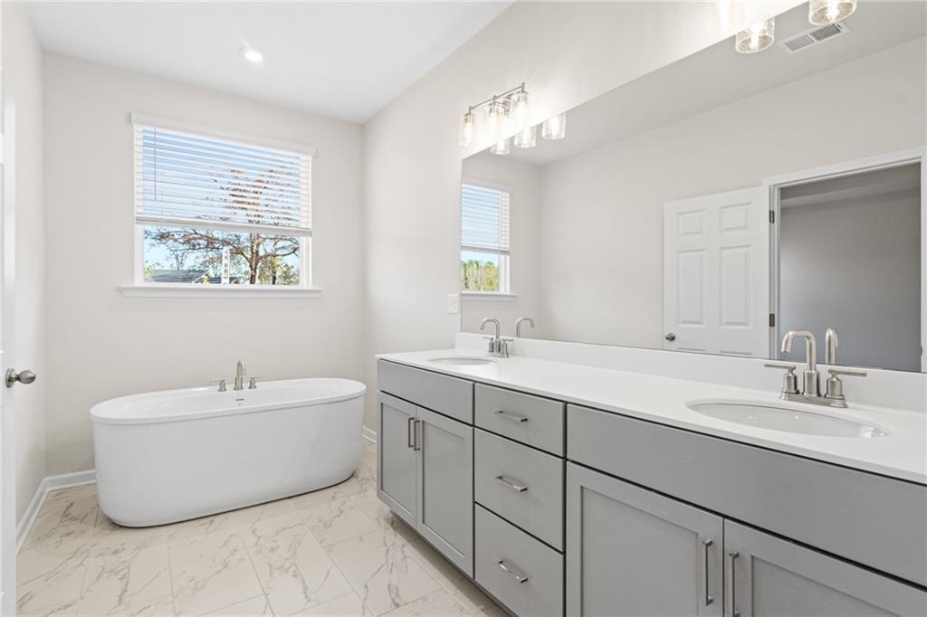 Modern primary bathroom with soaking tub and dual vanity in The Glenwood A at Wehunt Meadows, Hoschton, Georgia.