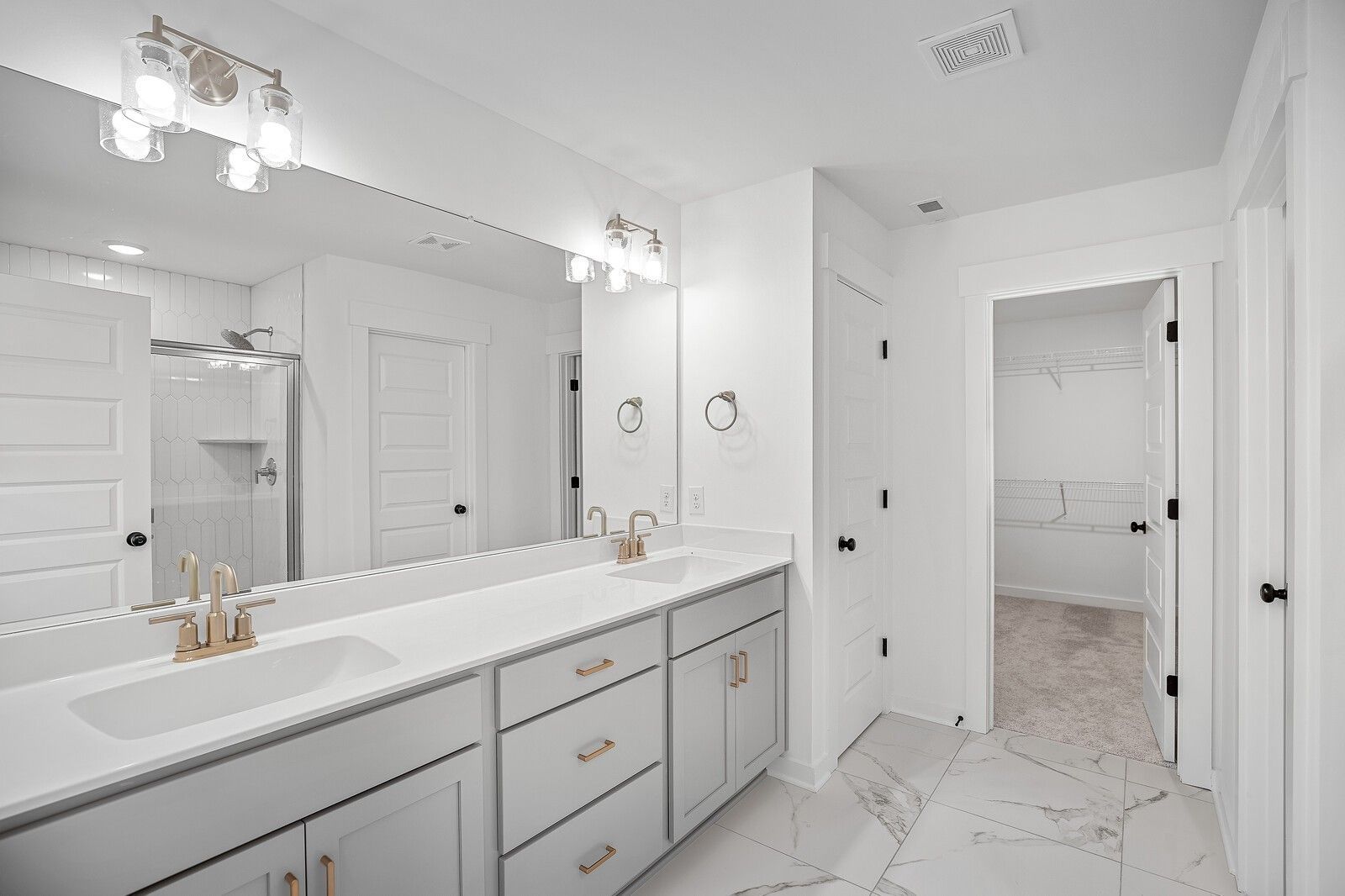 Elegant master bathroom with double vanity, gold fixtures, mirrors, and marble-look tile in Davidson Homes Logan C, Gallatin, TN