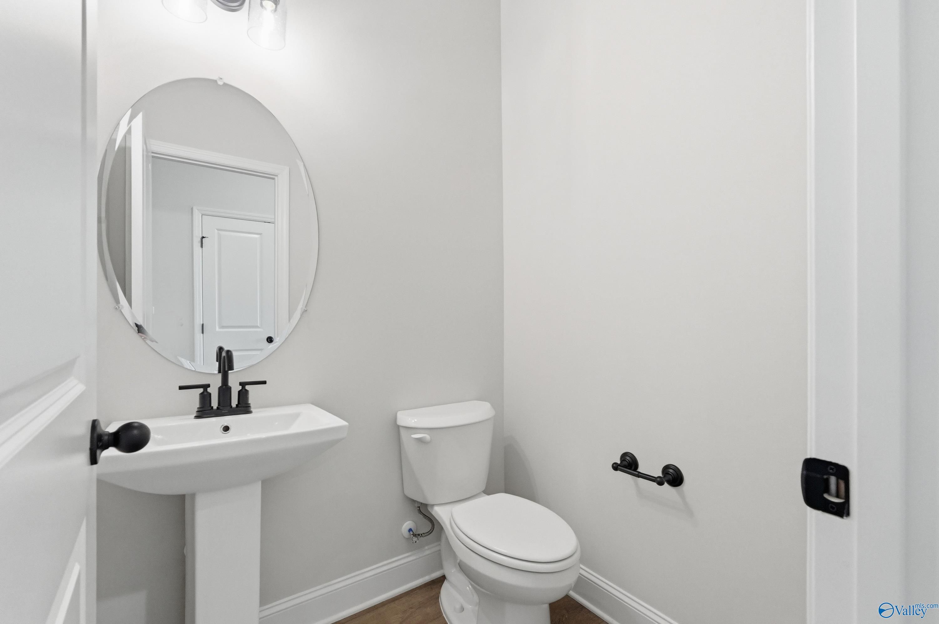 Elegant powder room with white pedestal sink, round mirror, black fixtures in Davidson Homes The Rockford B, The Meadows Athens AL