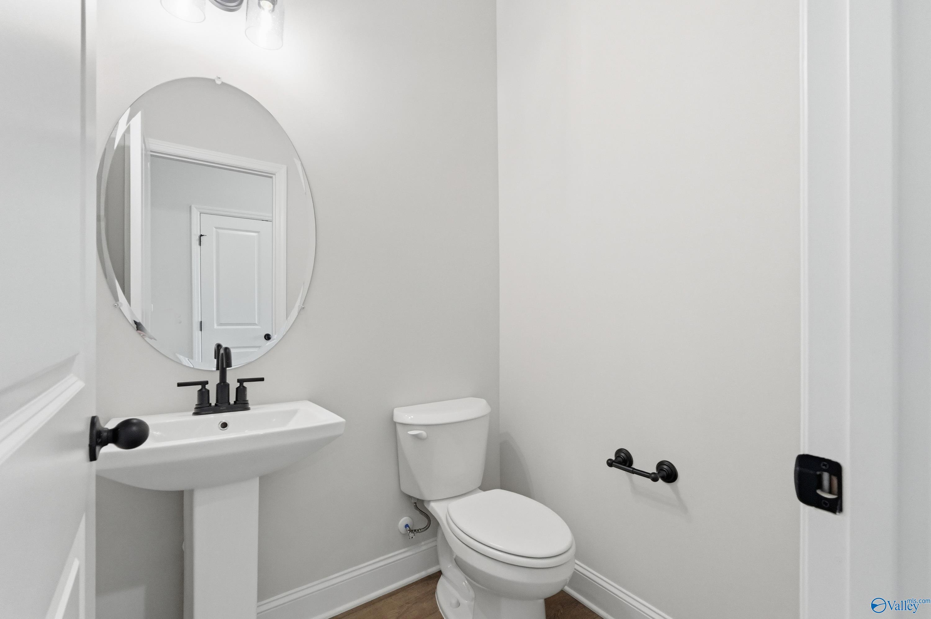 Elegant powder room with white pedestal sink, round mirror, black fixtures in Davidson Homes The Rockford B, The Meadows Athens AL