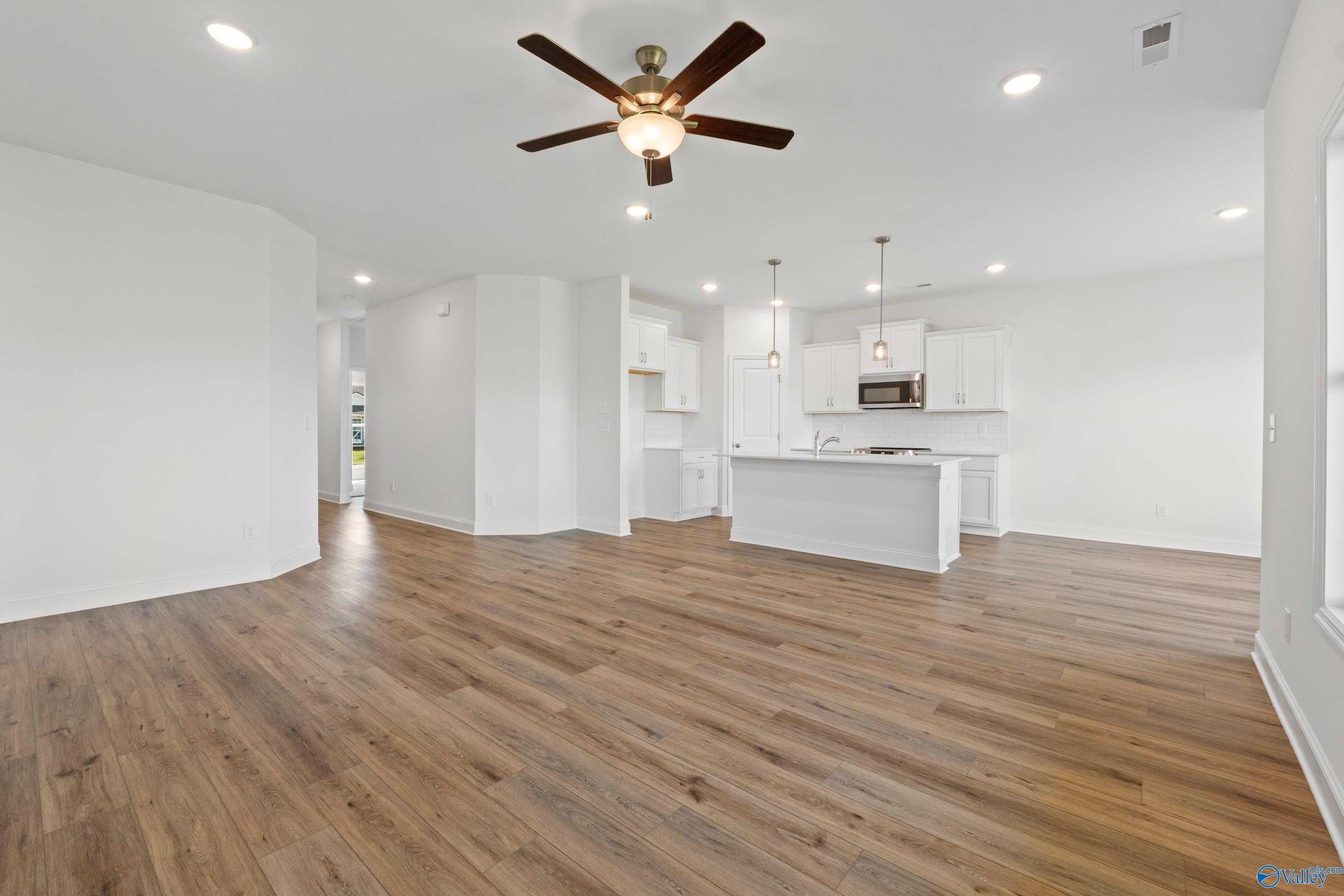 Open-concept kitchen and living area with white cabinetry, hardwood floors, and ceiling fan in Davidson Homes The Asheville C, Hazel Green, Alabama
