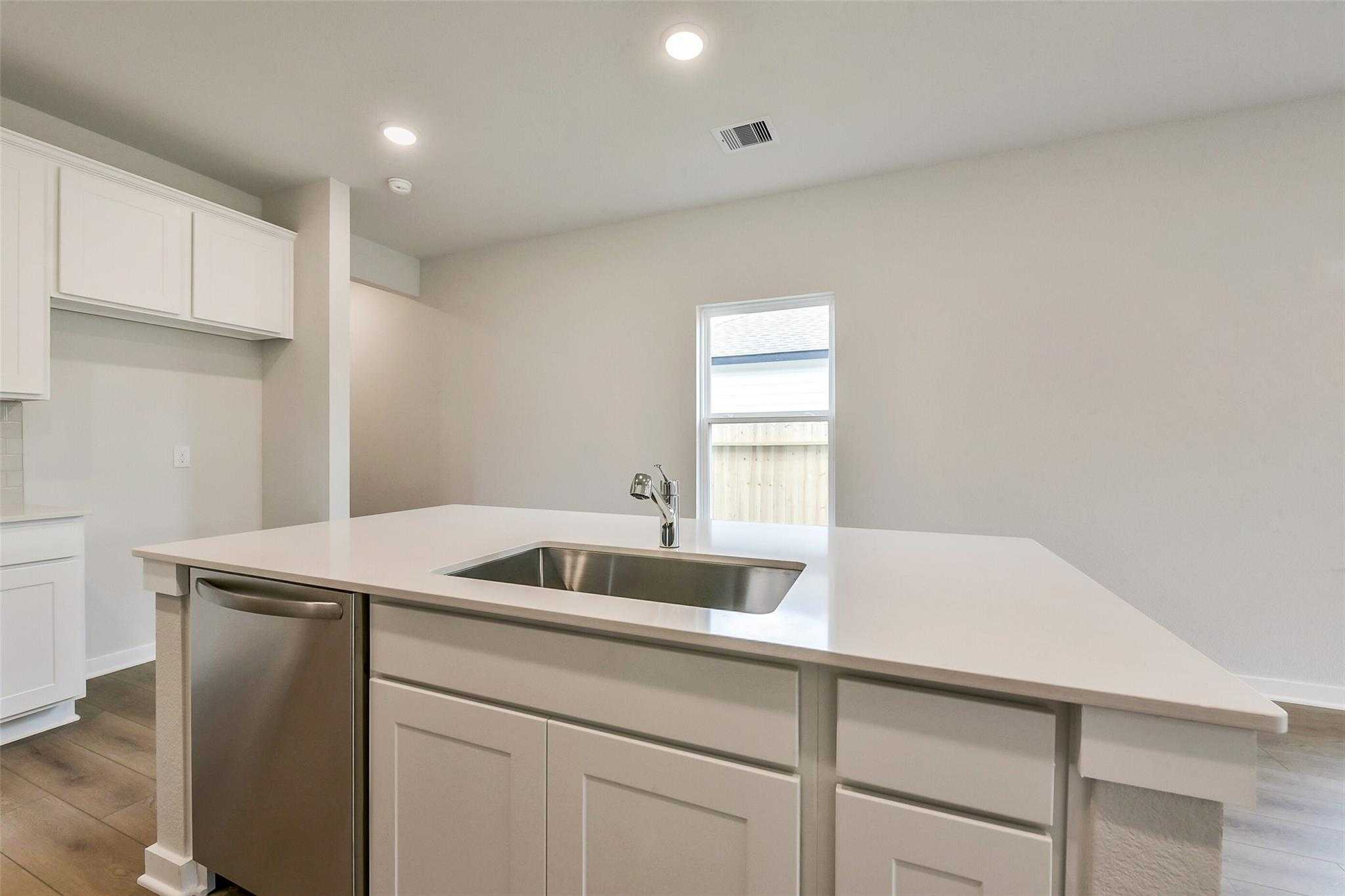 Modern white kitchen island with quartz countertop, stainless dishwasher, and undermount sink in The Frio G by Davidson Homes, Dayton, TX