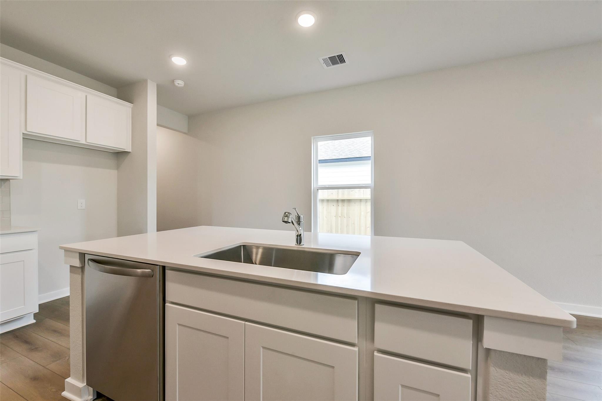 Modern white quartz kitchen island with undermount sink, stainless dishwasher, and backyard window in Davidson Homes The Frio G, Dayton TX