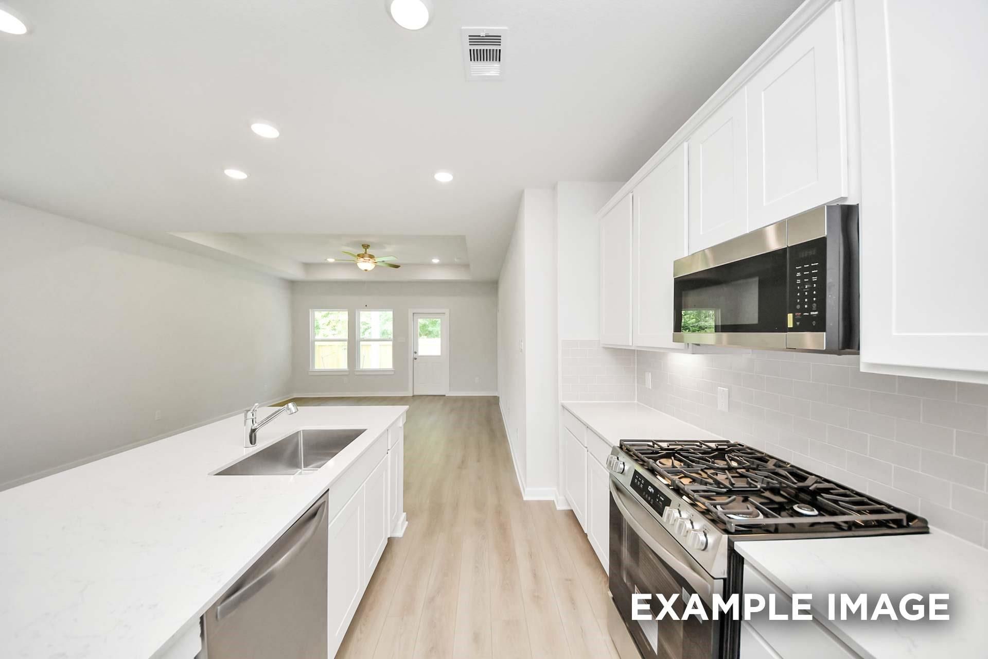 Bright white kitchen with island, stainless gas range, and open living area in Davidson Homes Blanco E, Windmill Estates, Magnolia, TX