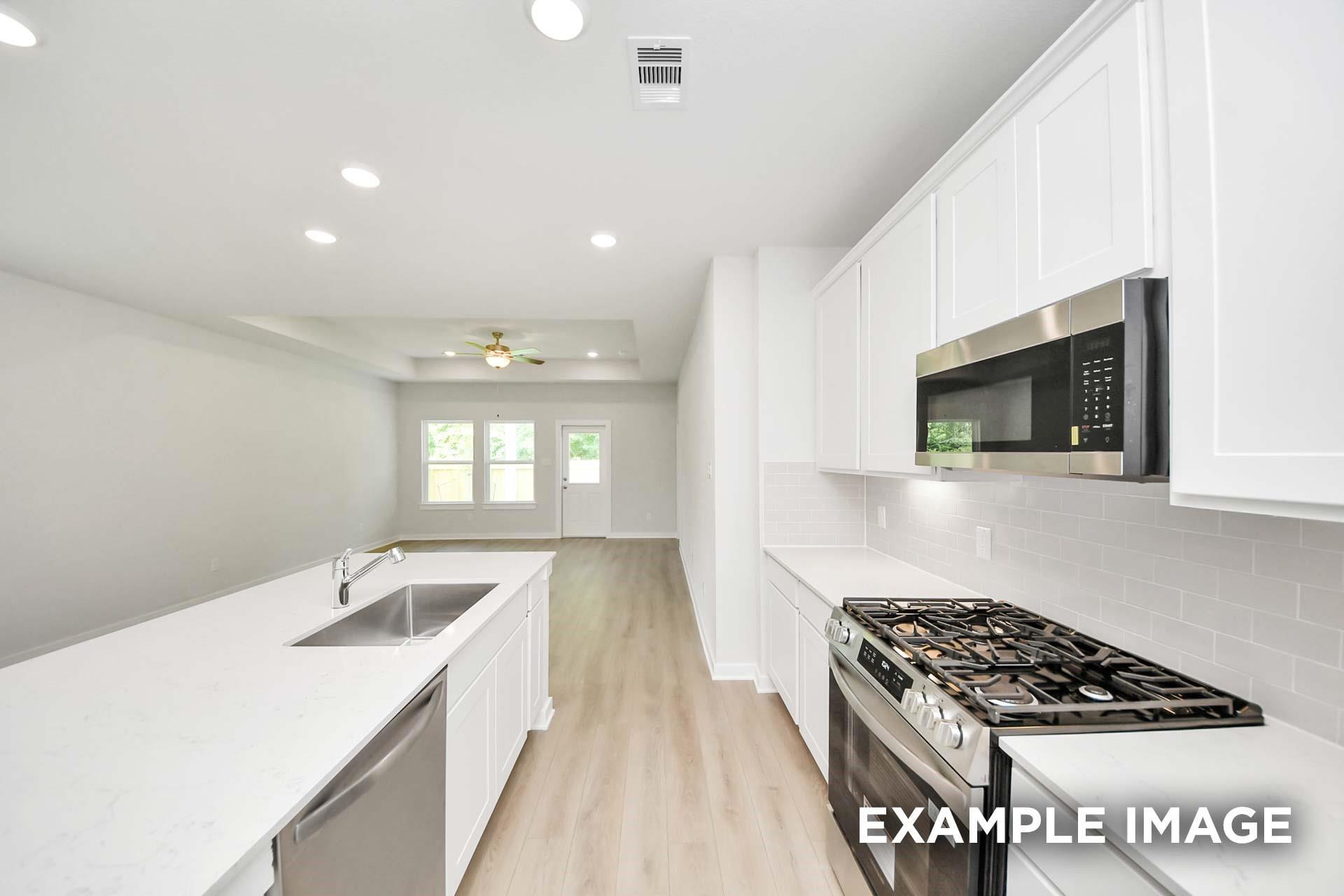 Bright white kitchen with island, stainless gas range, and open living area in Davidson Homes Blanco E, Windmill Estates, Magnolia, TX