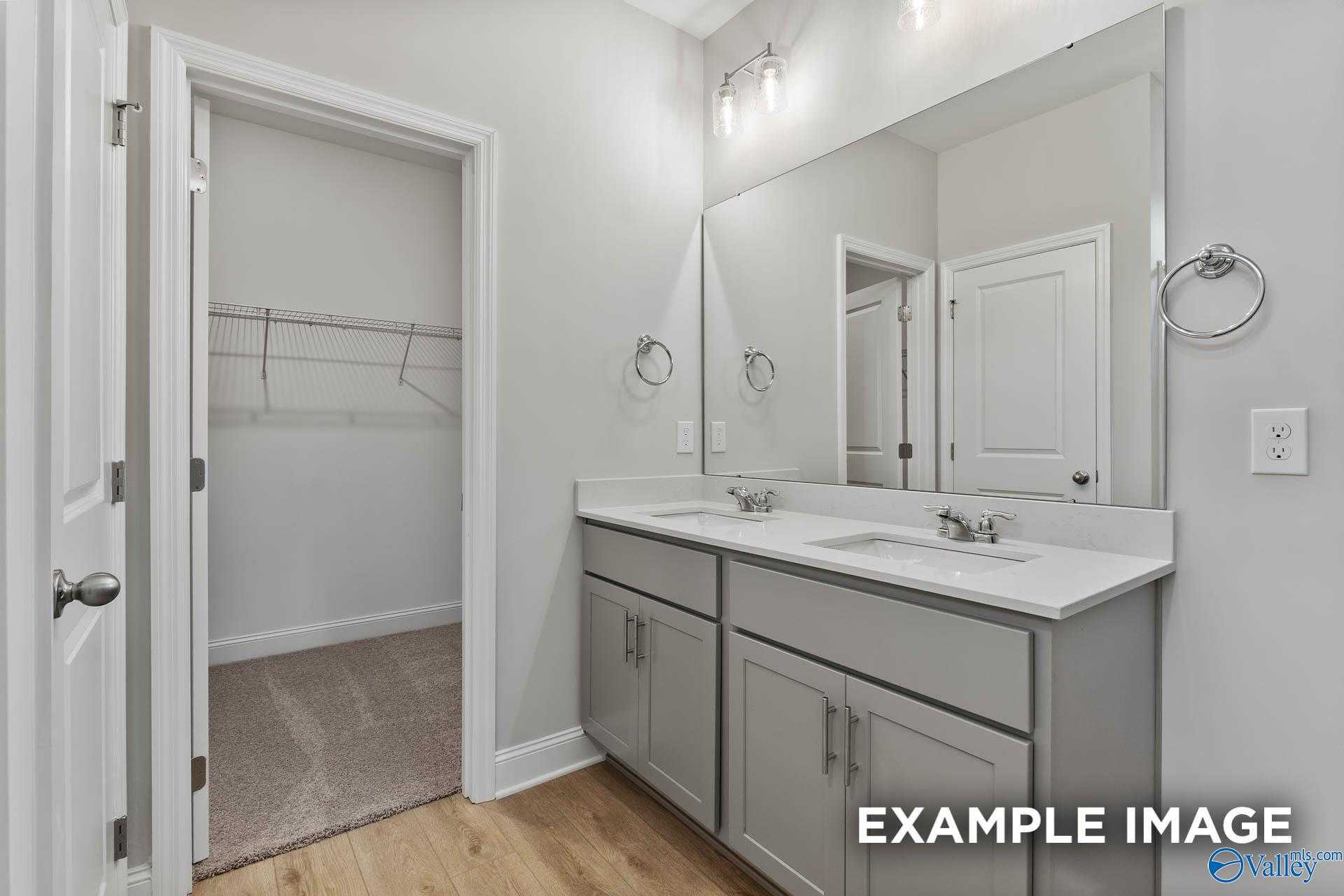 Elegant master bathroom with double vanity, gray cabinets, large mirror, and walk-in closet in Davidson Homes The Franklin C, Athens, Alabama