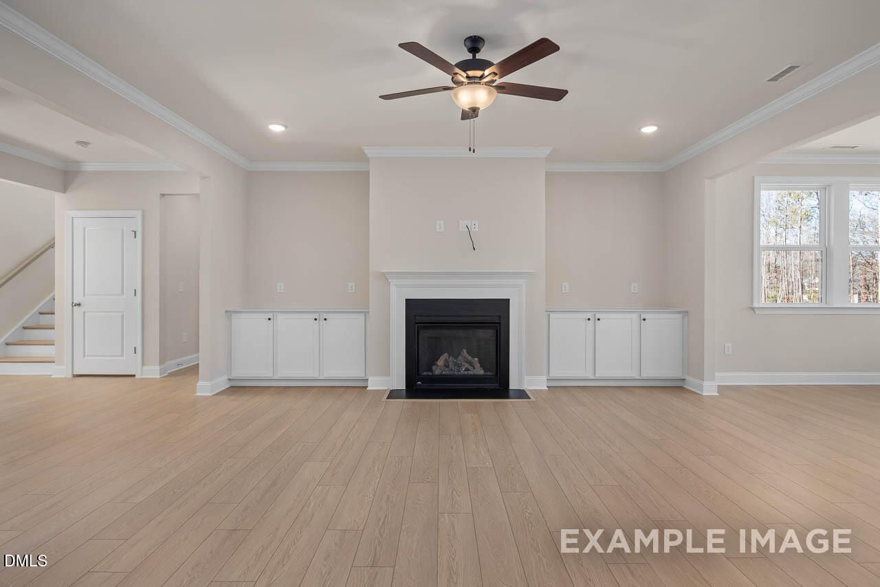 Cozy family room featuring gas fireplace, built-in cabinets, ceiling fans, and hardwood floors in Davidson Homes The Crawford D, Angier, NC