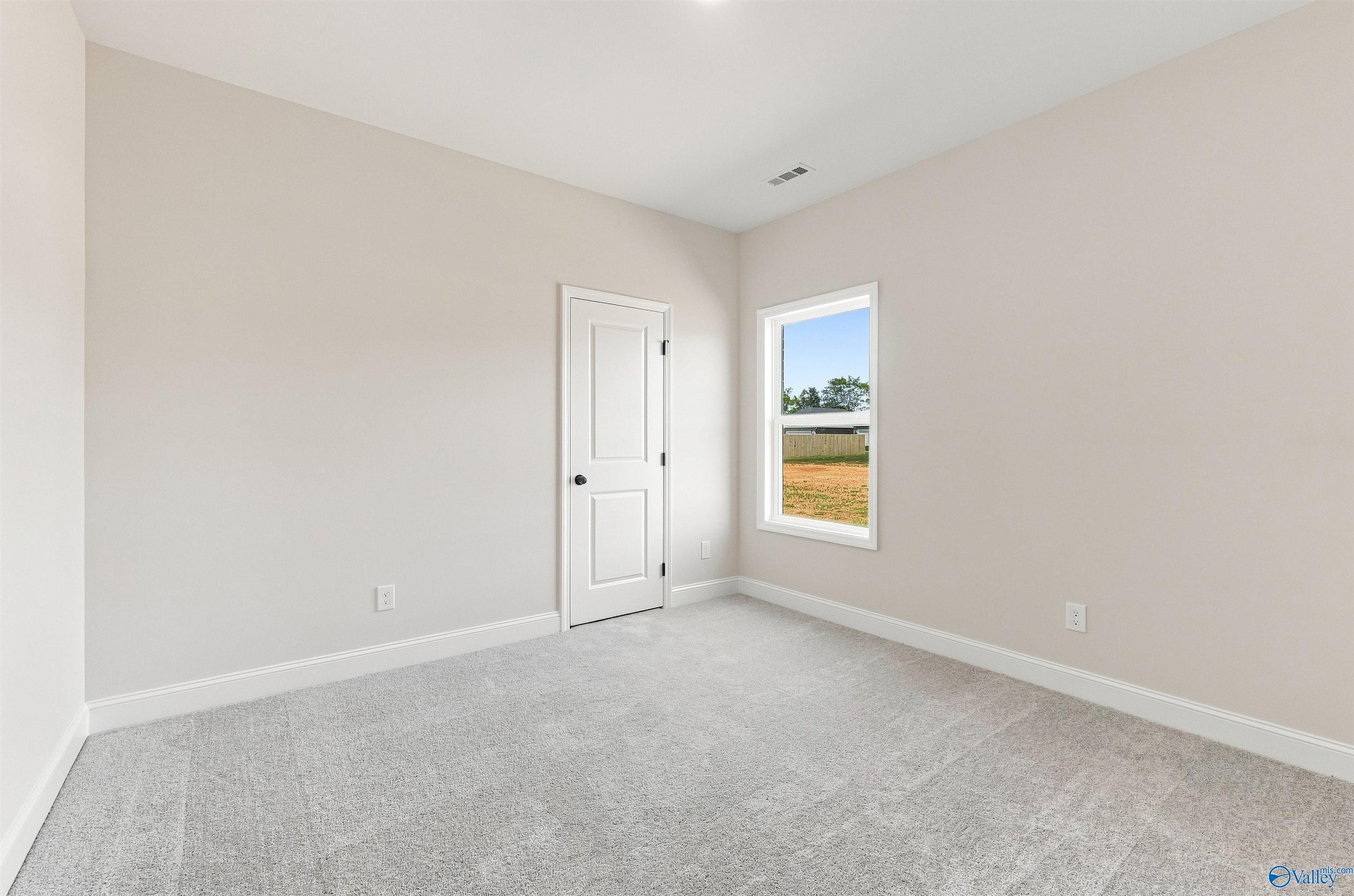 Bright empty bedroom with neutral walls, plush carpet, and white door in Davidson Homes The Everett B plan, Ivy Hills, Toney, Alabama