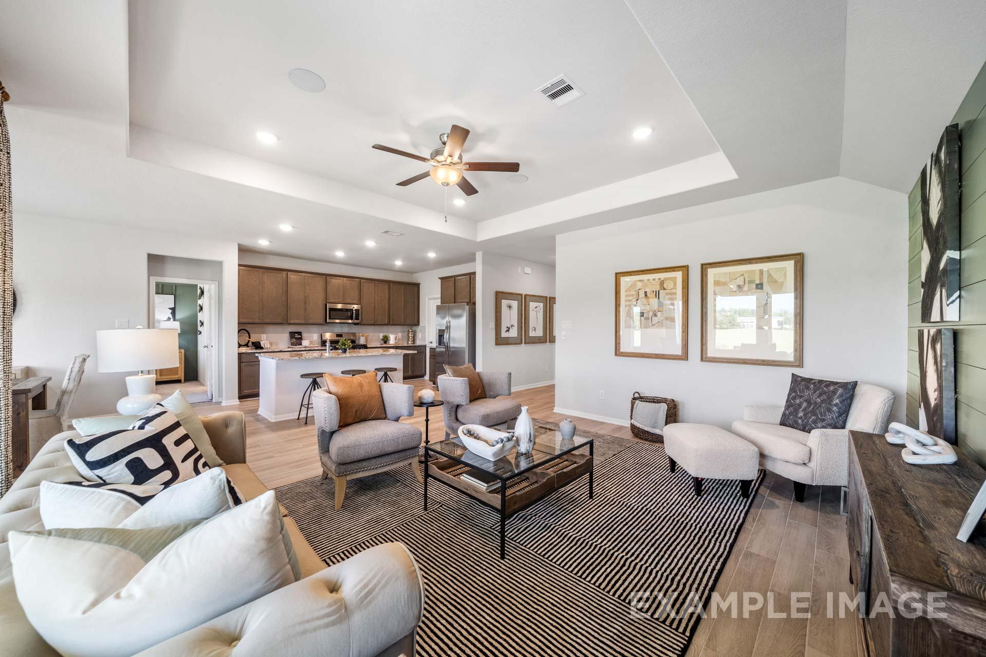 Open-concept living room and kitchen in The Acadia A 4-bedroom home, Rosharon TX, featuring beige sofas, wood floors, and ceiling fan