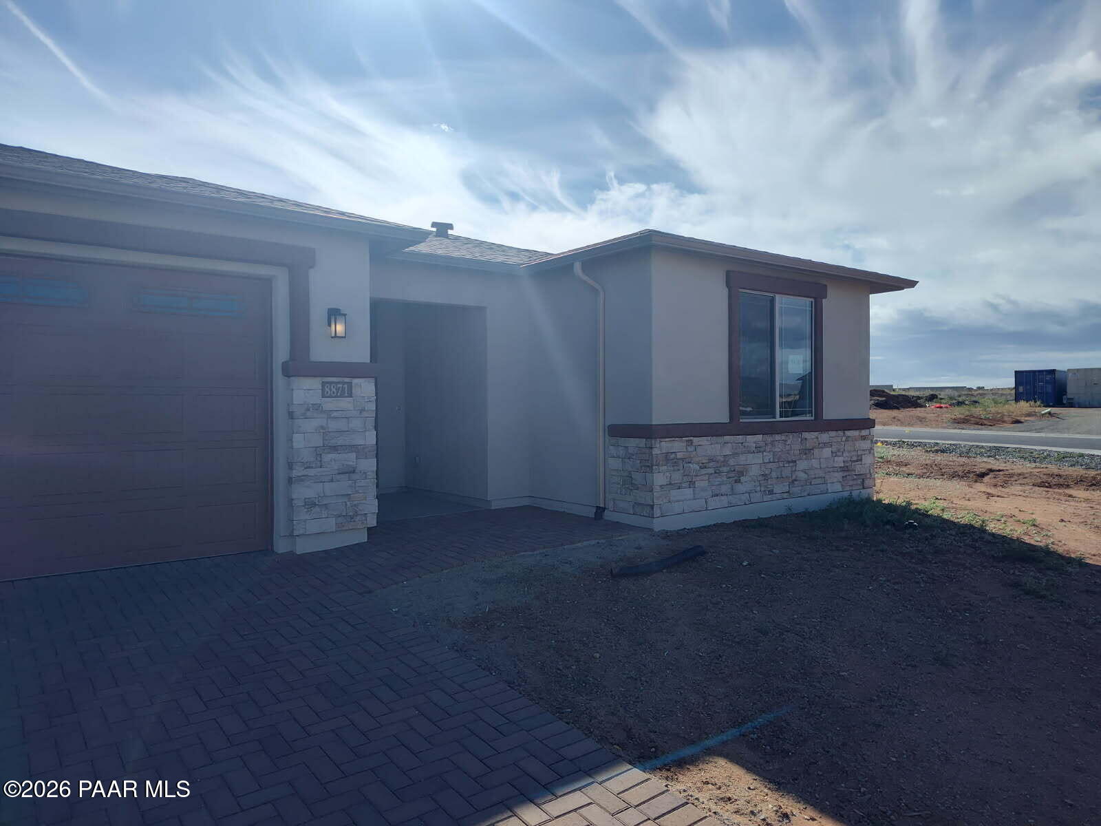 Modern beige stucco single-story home with 3-car garage, stone accents, and paver walkway in North Ridge at Pronghorn Ranch, Prescott Valley, Arizona