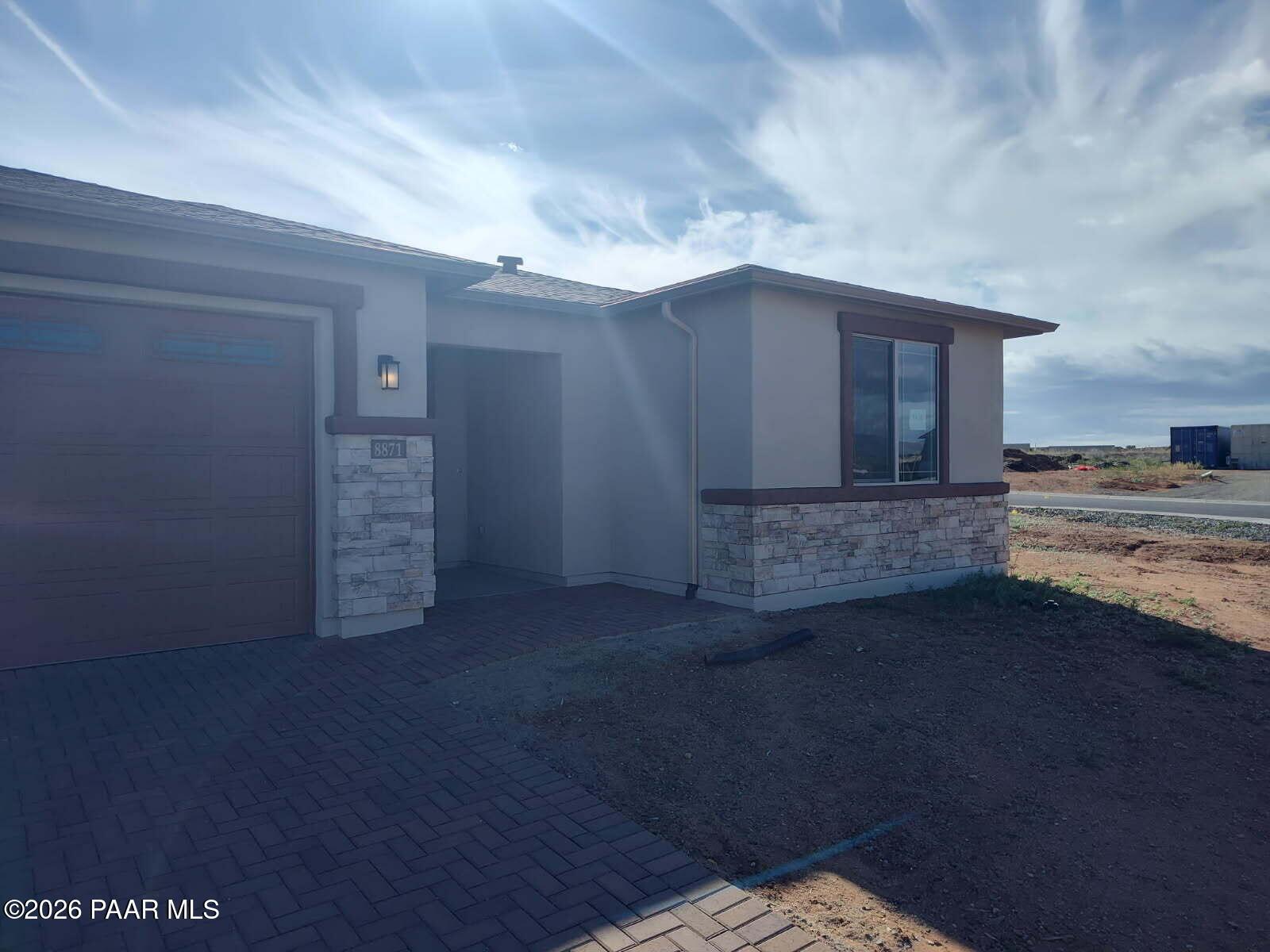 Modern beige stucco single-story home with 3-car garage, stone accents, and paver walkway in North Ridge at Pronghorn Ranch, Prescott Valley, Arizona