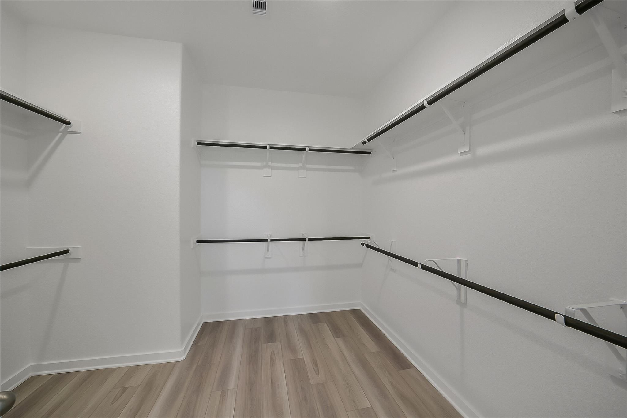 Spacious walk-in closet with built-in shelves, hanging rods, and wood-look flooring in Davidson Homes The Acadia A, Sunterra, Katy, Texas