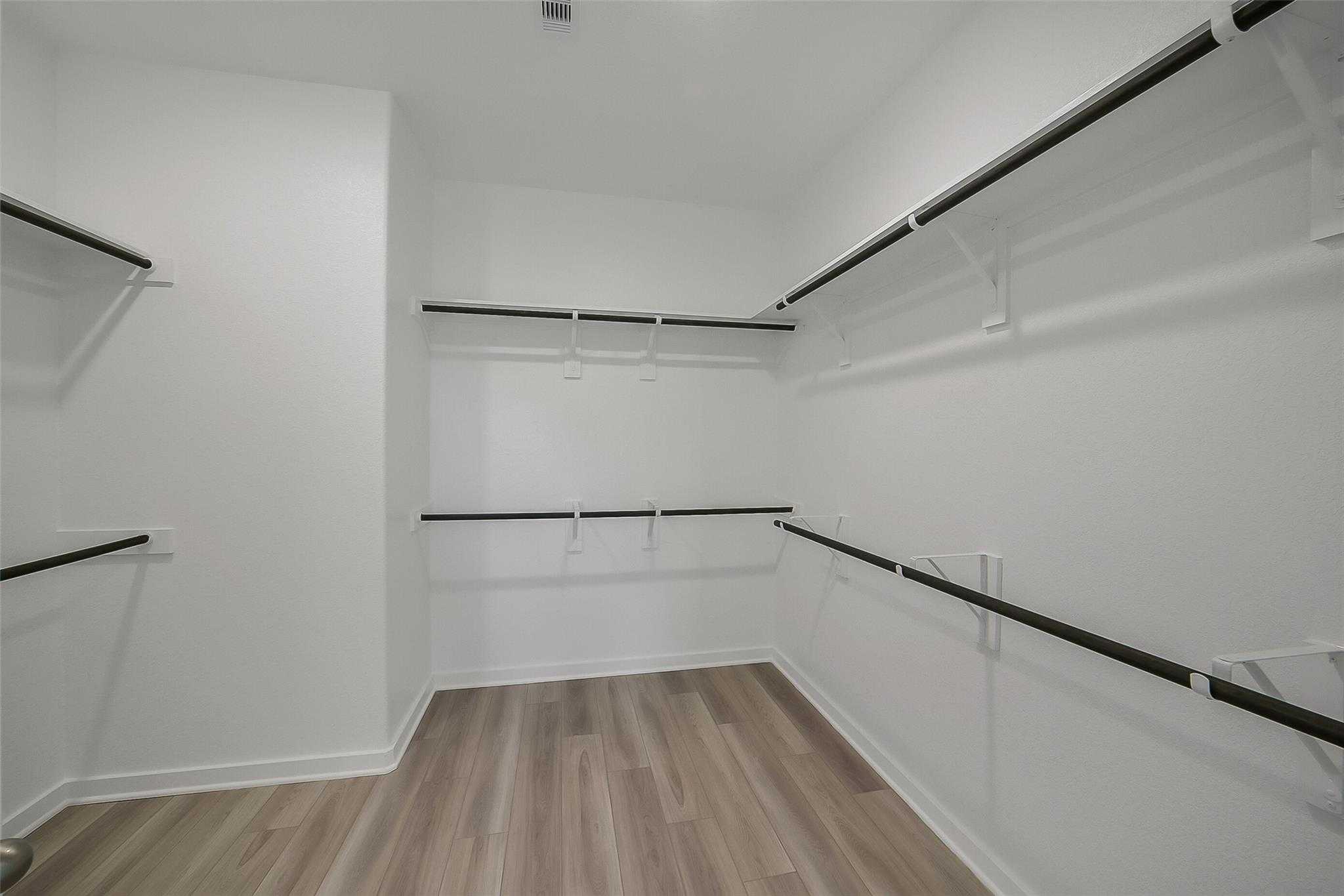 Spacious walk-in closet with built-in shelves, hanging rods, and wood-look flooring in Davidson Homes The Acadia A, Sunterra, Katy, Texas