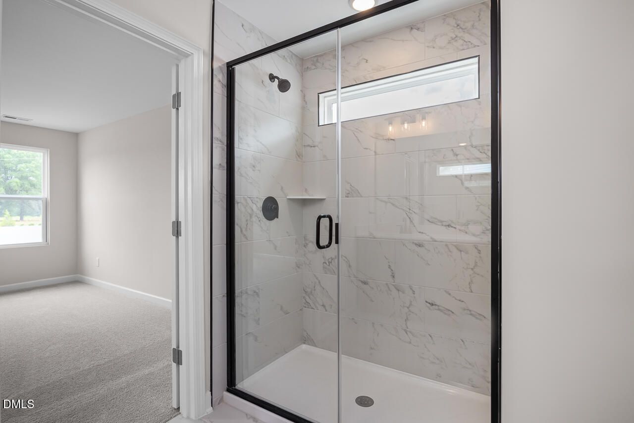 Modern walk-in shower with marble-look tile in a Davidson Homes The Willow B floor plan in Zebulon, North Carolina.