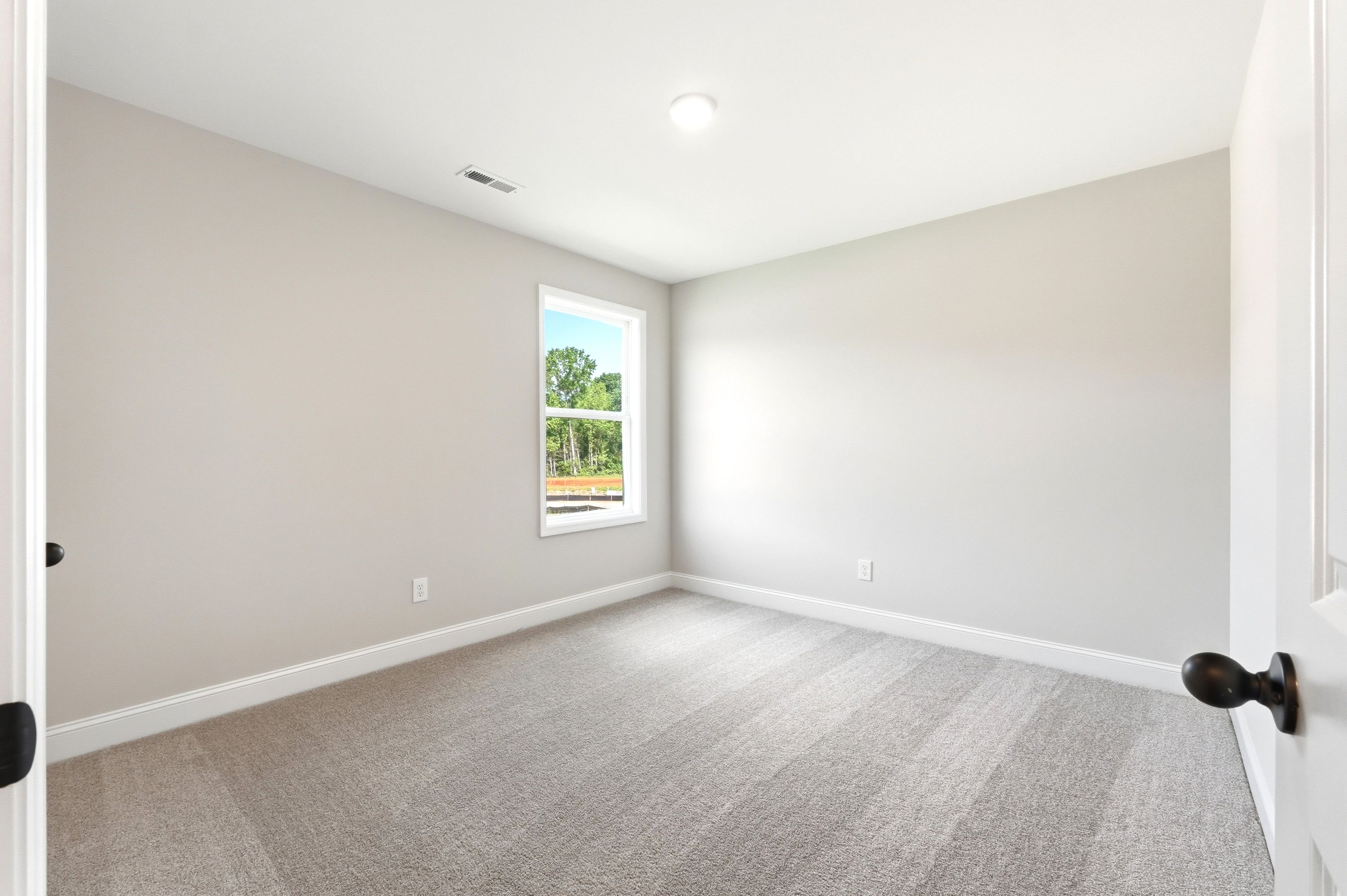Spacious secondary bedroom with neutral carpet and natural lighting in The Russell A home design by Davidson Homes.