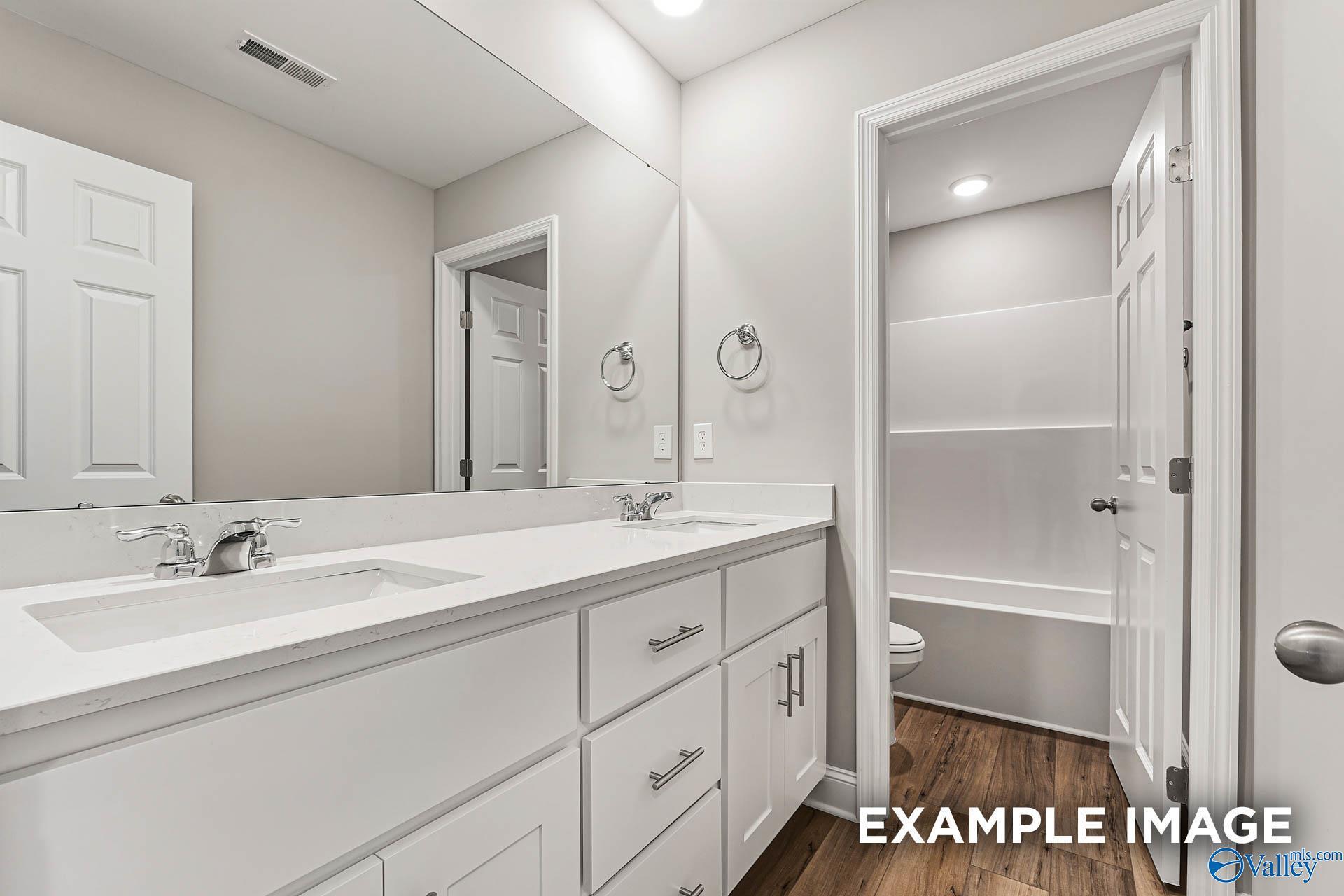 Modern double vanity bathroom with white quartz counters, chrome faucets, and adjacent tub in Chelsea B home, Toney Alabama