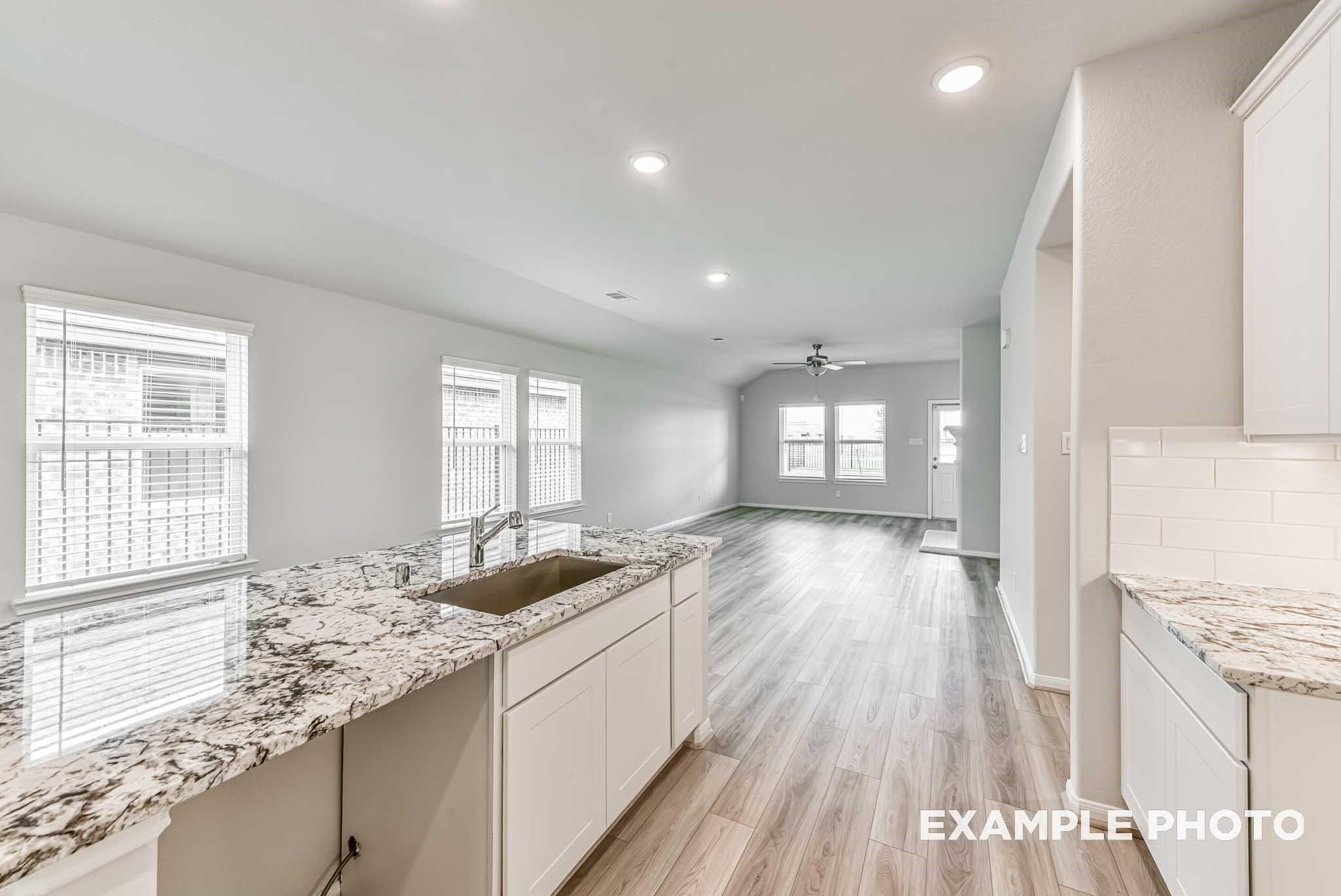 Modern open-concept kitchen with white shaker cabinets, granite countertops, and stainless sink in Davidson Homes The Riviera A, Rosharon, TX