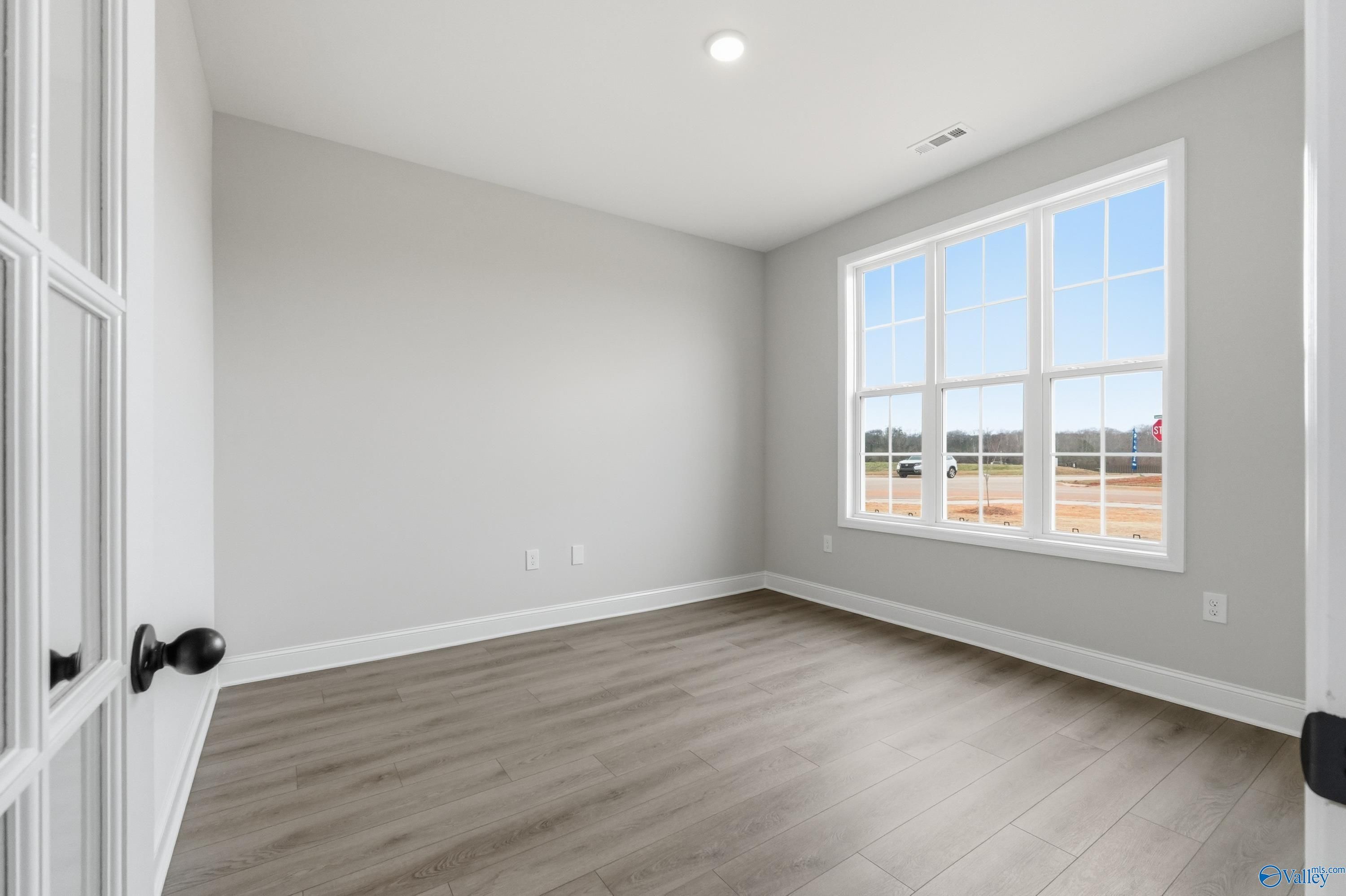 Bright secondary bedroom with large triple windows, gray walls, and luxury vinyl plank floors in Davidson Homes The Finleigh, Meridianville, Alabama