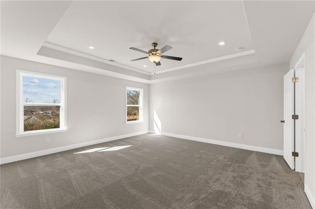 Bright bedroom with tray ceiling, ceiling fan, gray carpet, and large windows in Davidson Homes The Willow B, Hoschton, GA