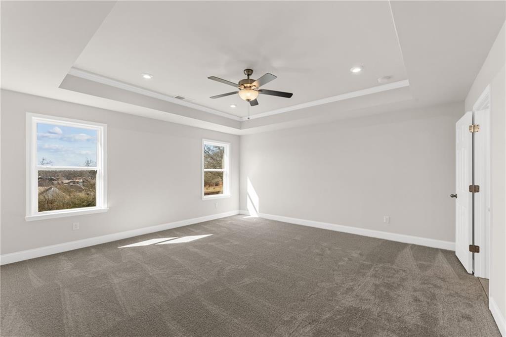 Bright bedroom with tray ceiling, ceiling fan, gray carpet, and large windows in Davidson Homes The Willow B, Hoschton, GA