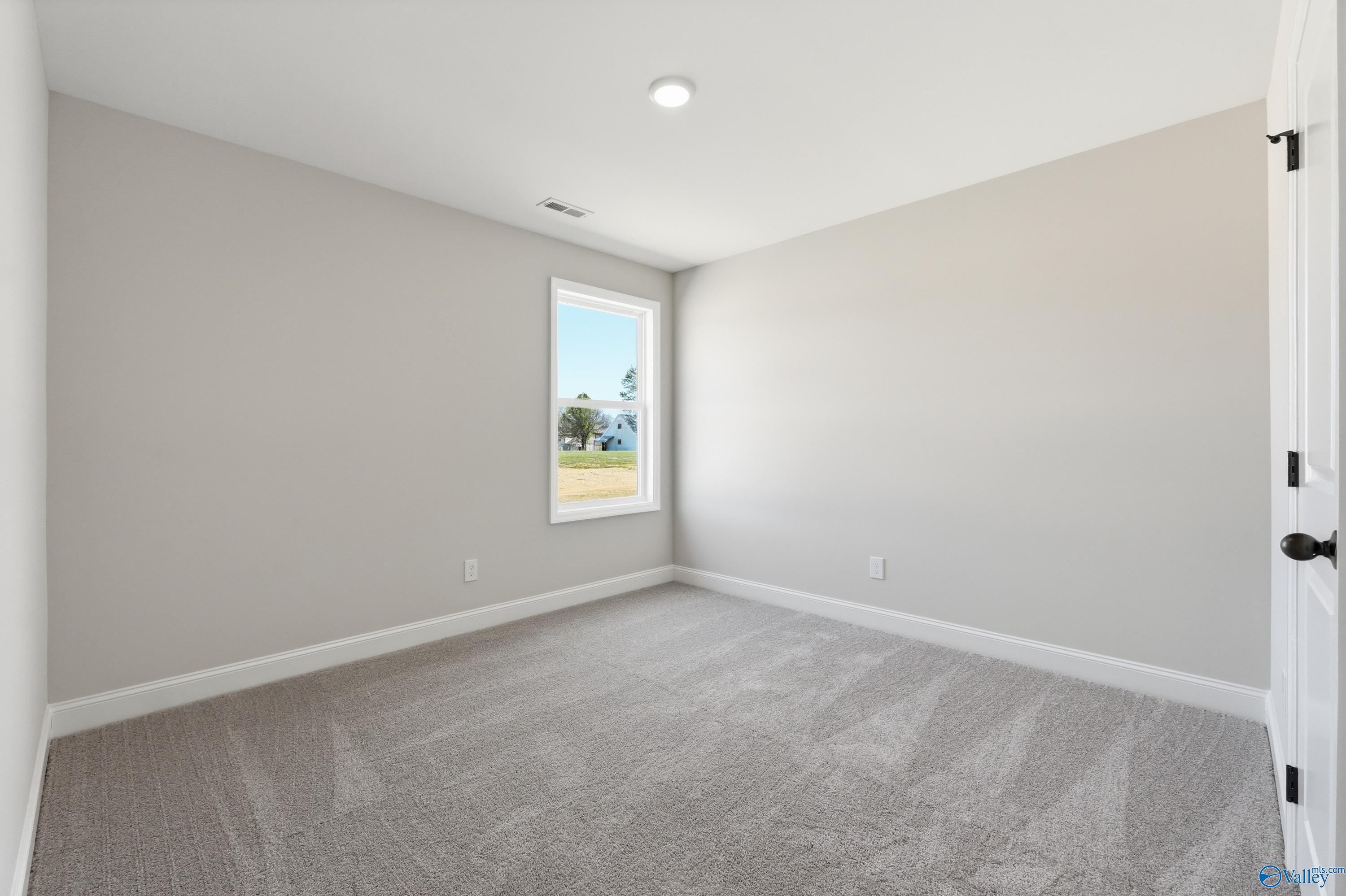 Bright secondary bedroom with light gray walls, plush carpet, and window view in Davidson Homes The Franklin V, Athens, Alabama