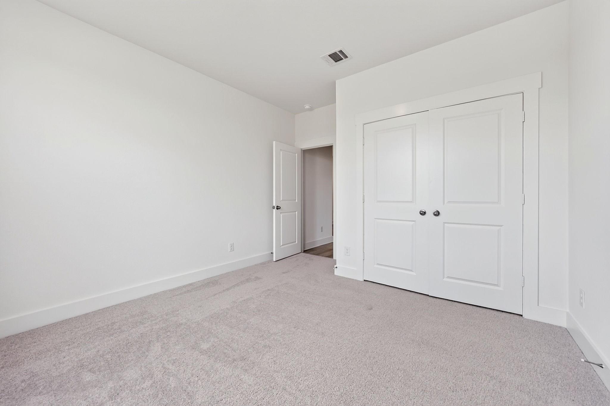 Bright bedroom with plush carpet, white walls, and double-door closet in Davidson Homes' The Holly F, Josephine, Texas