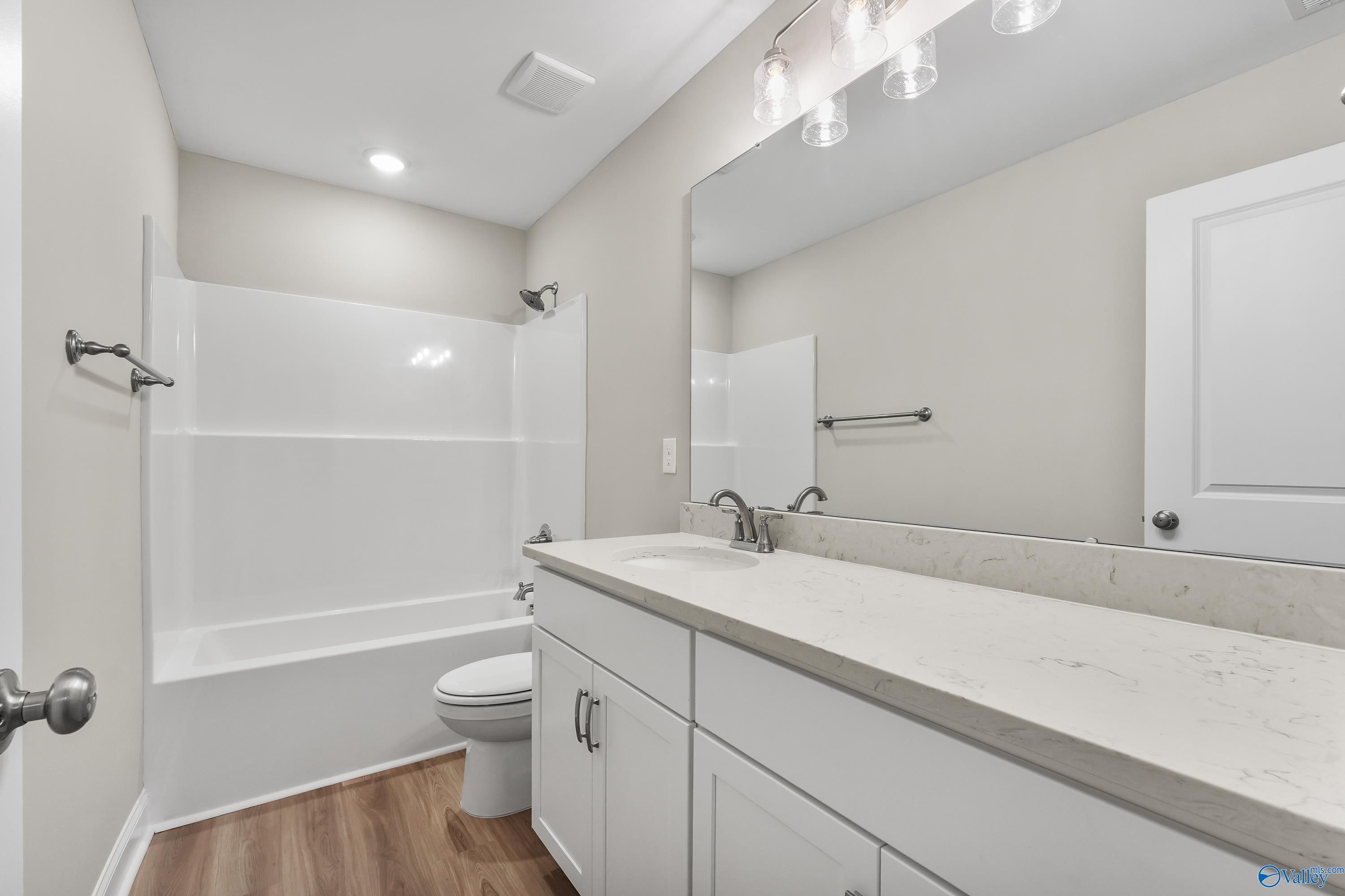 Modern bathroom with white tub-shower combo, quartz vanity, and frameless mirror in Evermore Homes The Haven, Owens Cross Roads, AL