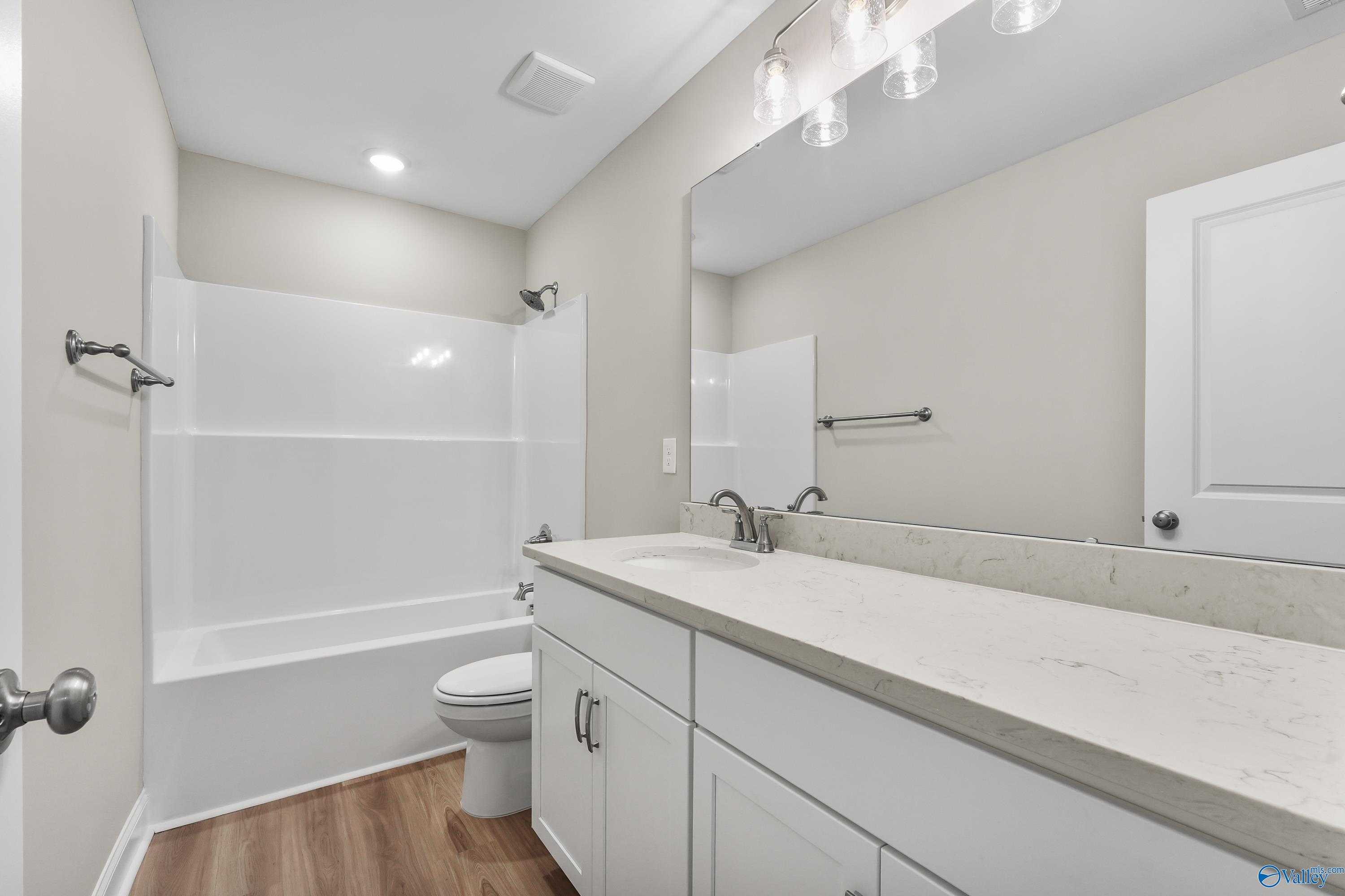Modern bathroom with white tub-shower combo, quartz vanity, and frameless mirror in Evermore Homes The Haven, Owens Cross Roads, AL