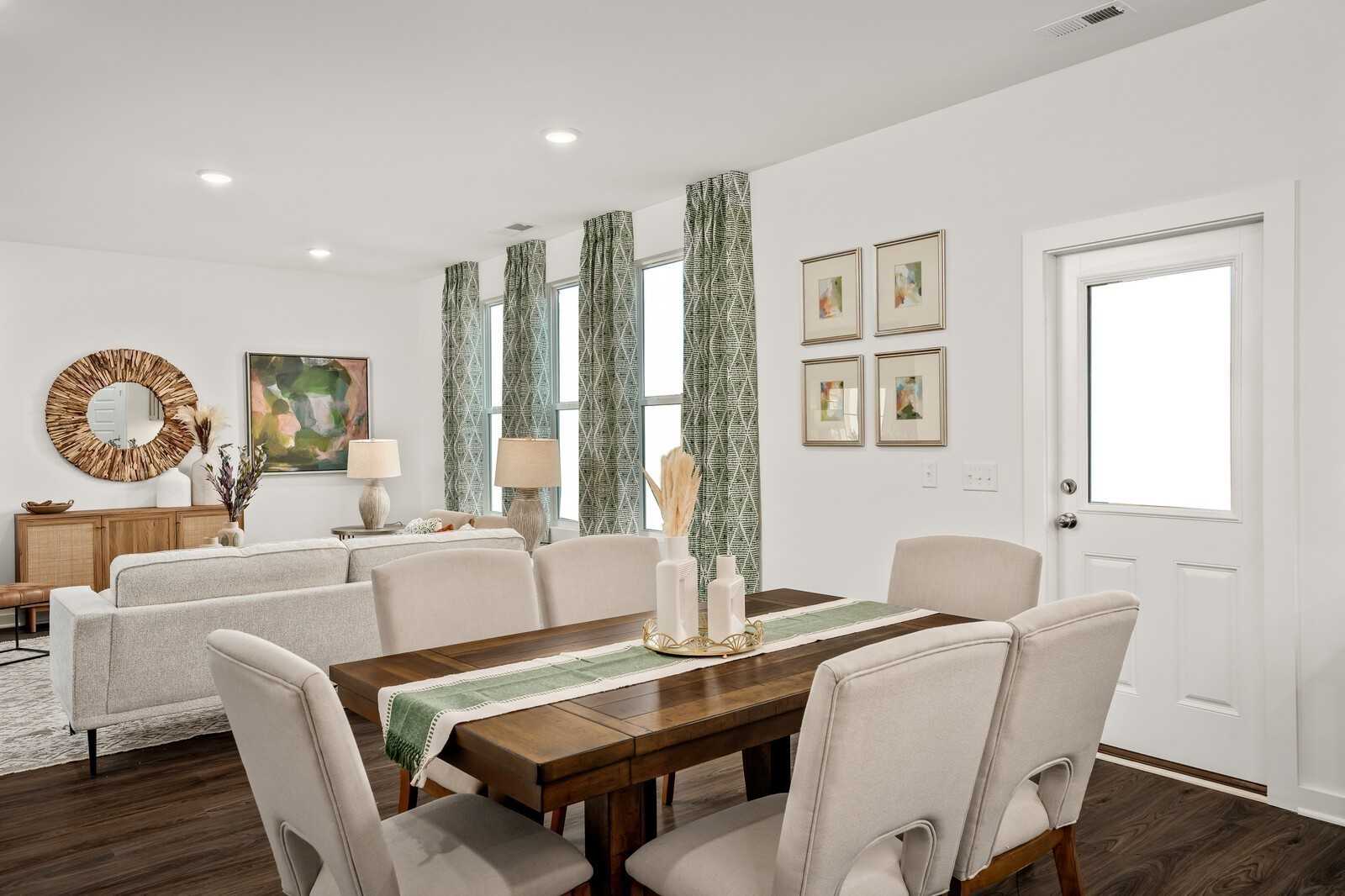 Elegant dining room featuring wooden table with runner, beige chairs, rattan mirror, and large curtained windows in Davidson Homes The Gordon C, Sage Farms, White House, Tennessee