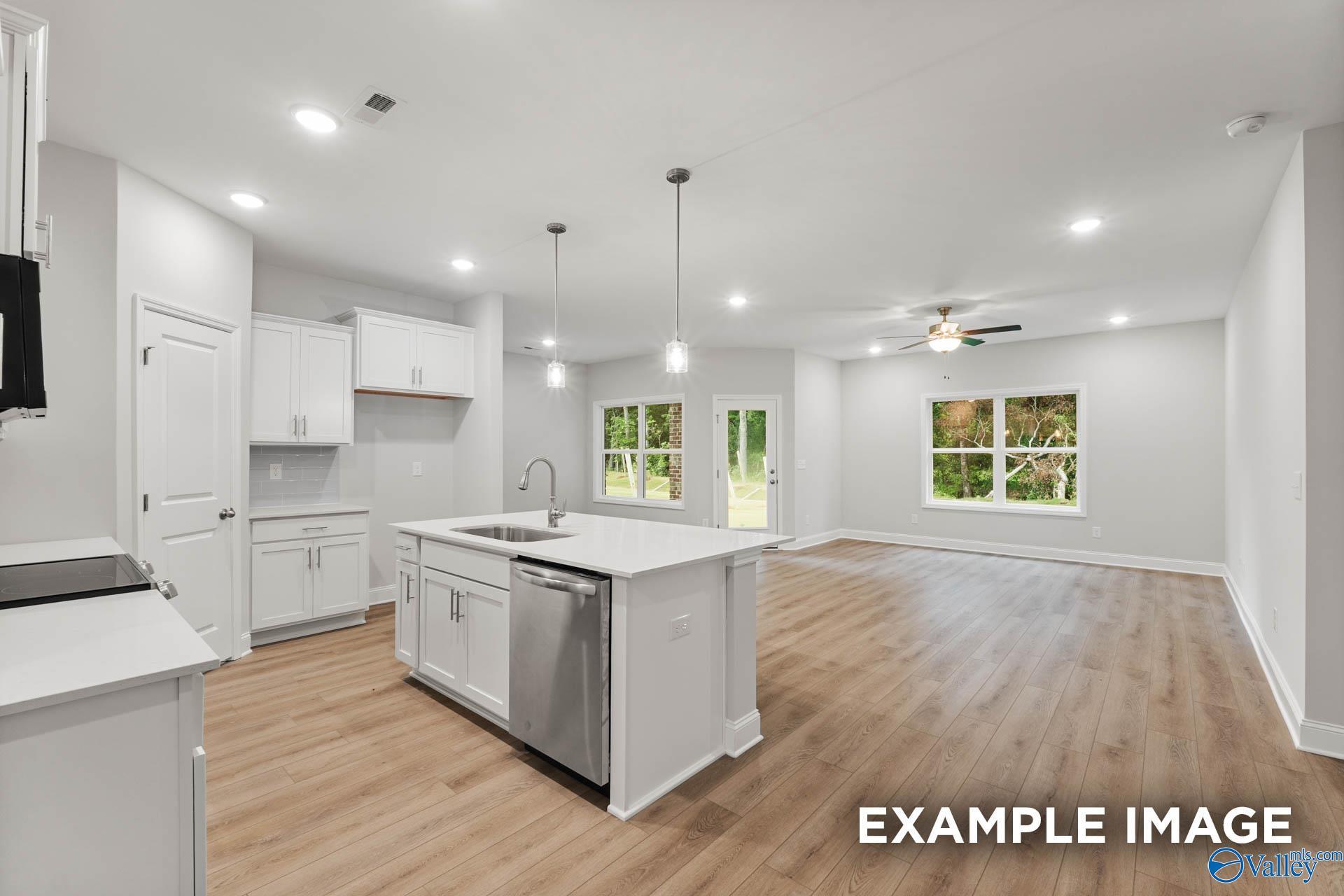Open-concept kitchen with white island, stainless appliances, hardwood floors, and backyard views in Davidson Homes The Daphne, Meridianville, Alabama